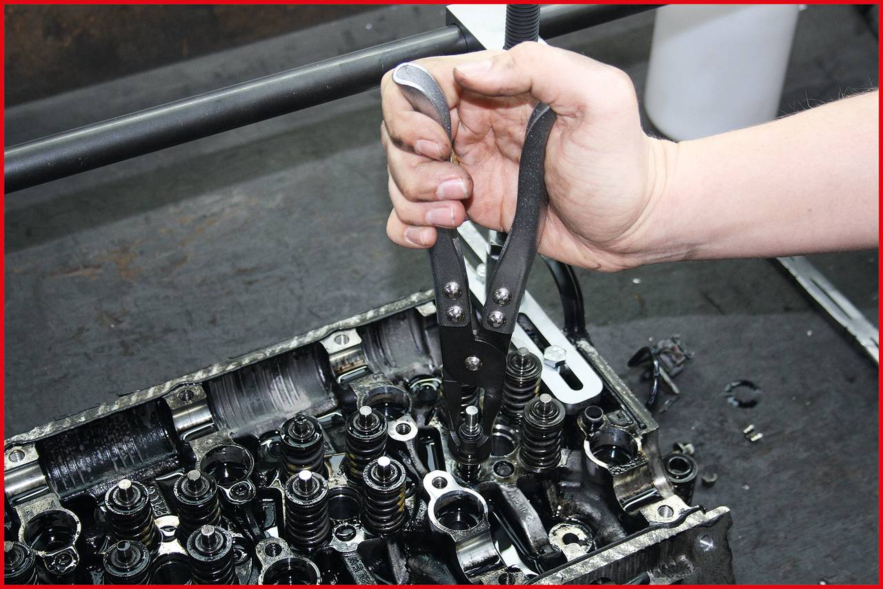 Ruka používa kliešte pri práci na zložitej časti motora. Niekoľko ventilov a mechanizmov je viditeľných.