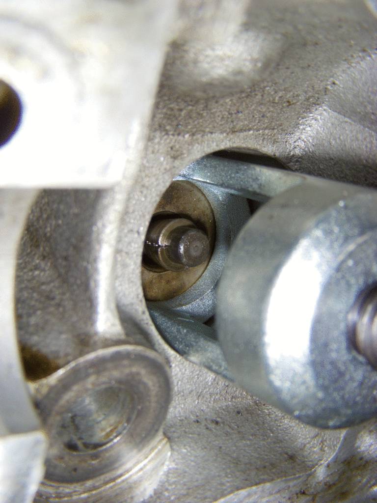 Detailný pohľad na kovový komponent v zložitom mechanickom systéme. Zameraný na skrutku a čap, ktoré sú kľúčové pre jeho funkčnosť.