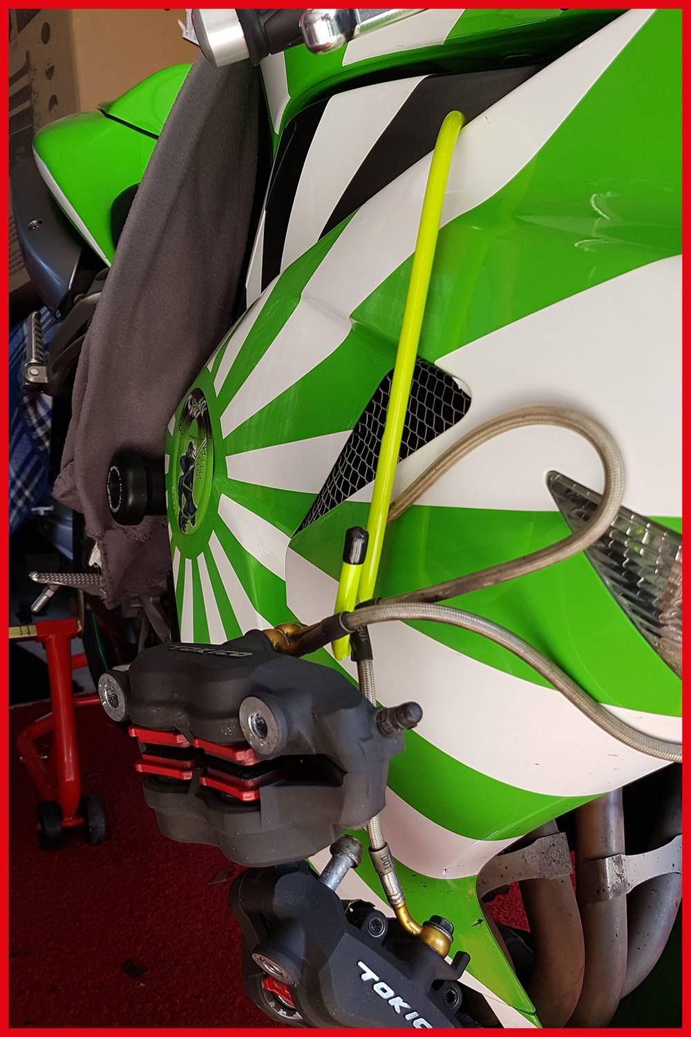 Zeleno-biely kryt športovej pretekárskej motorky s žltou brzdovou ventilačnou hadicou, červeným brzdovým strmeňom a viditeľným označením Tokico.