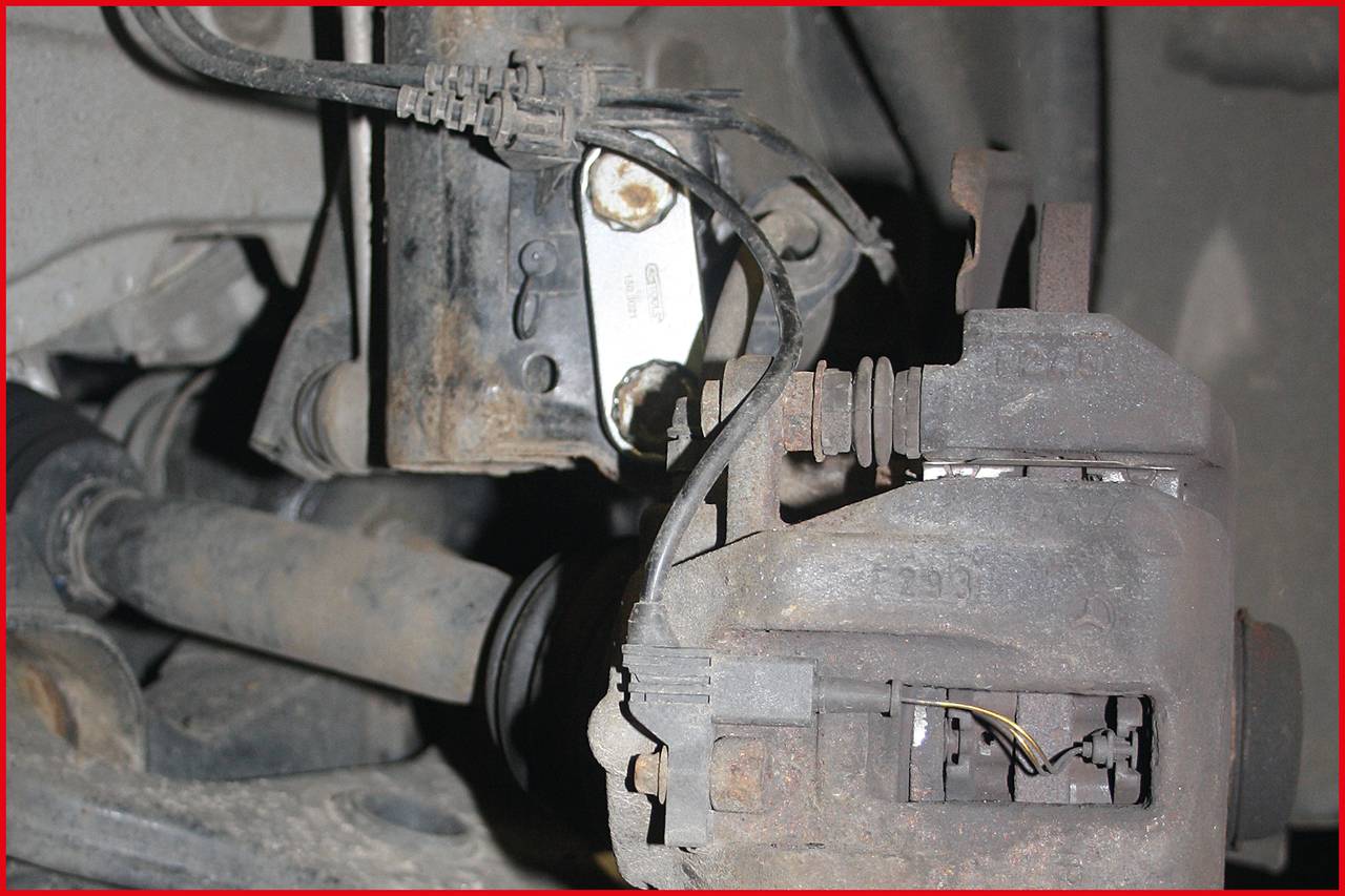 Detailný záber starej, zhrdzavenej brzdovej sústavy automobilu so všetkými viditelnými káblami a skrutkami, ktorý poukazuje na charakteristické detaily a opotrebenie.