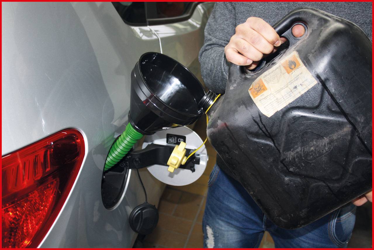 Osoba nalieva palivo z kanstra do nádrže automobilu. Čierny lievik pomáha pri nalievaní.
