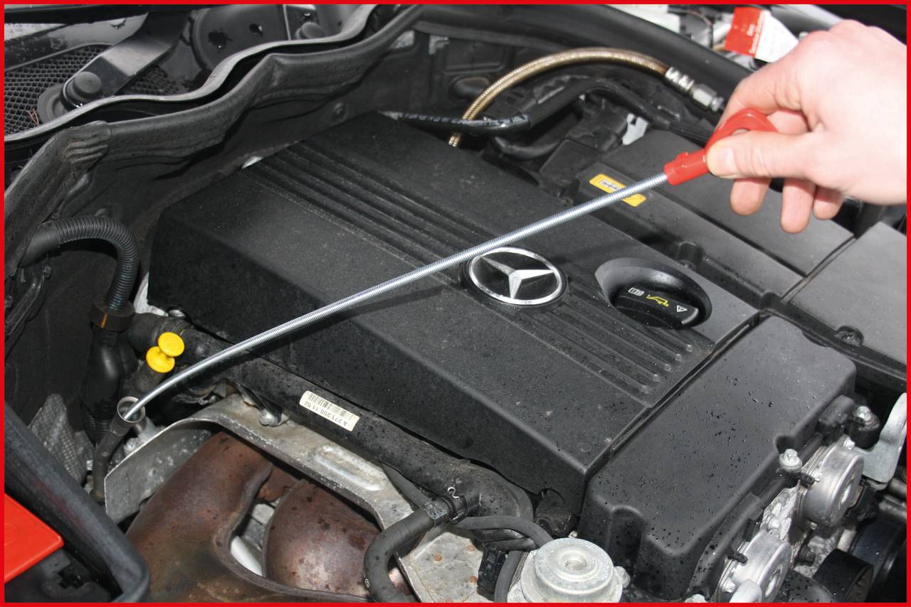 Otvorené auto, kde jedna osoba vyťahuje mierku oleja z motorového priestoru, aby skontrolovala hladinu oleja. Motor je čistý a dobre viditeľný.
