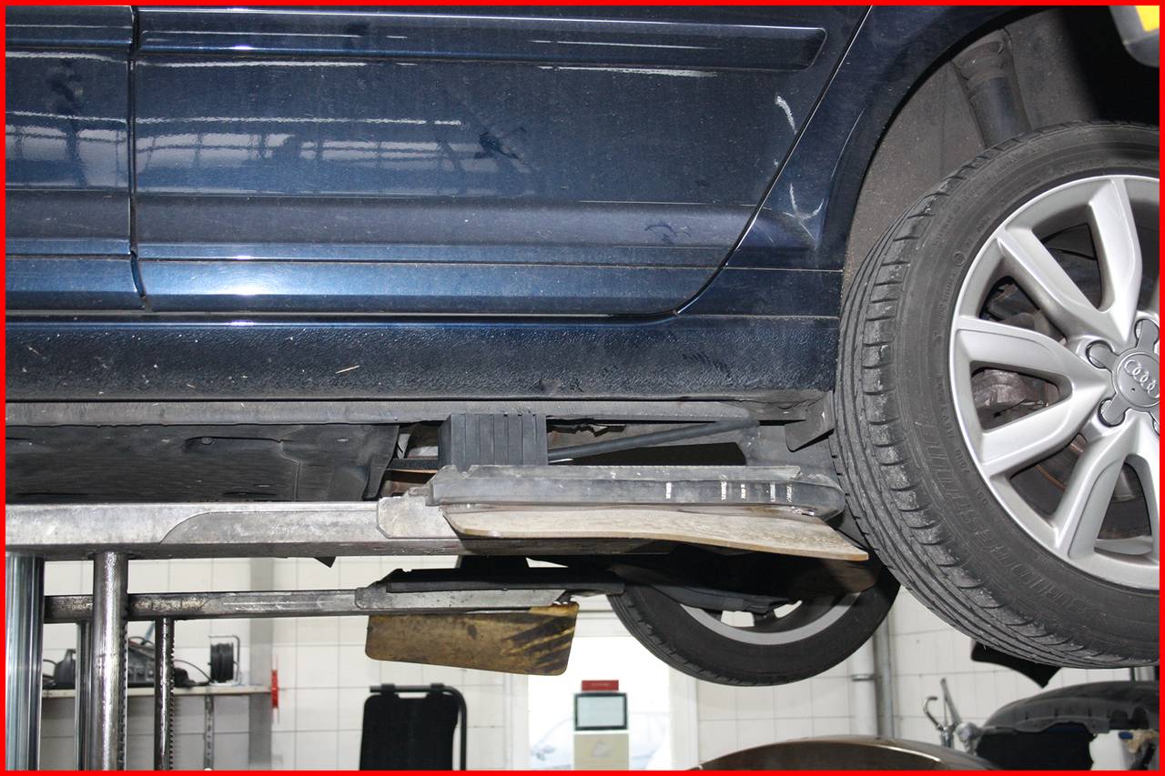 'Auto na zdviháku v servise, zameraný pohľad na koleso a spodok vozidla. Vykonávajú sa servisné práce.'