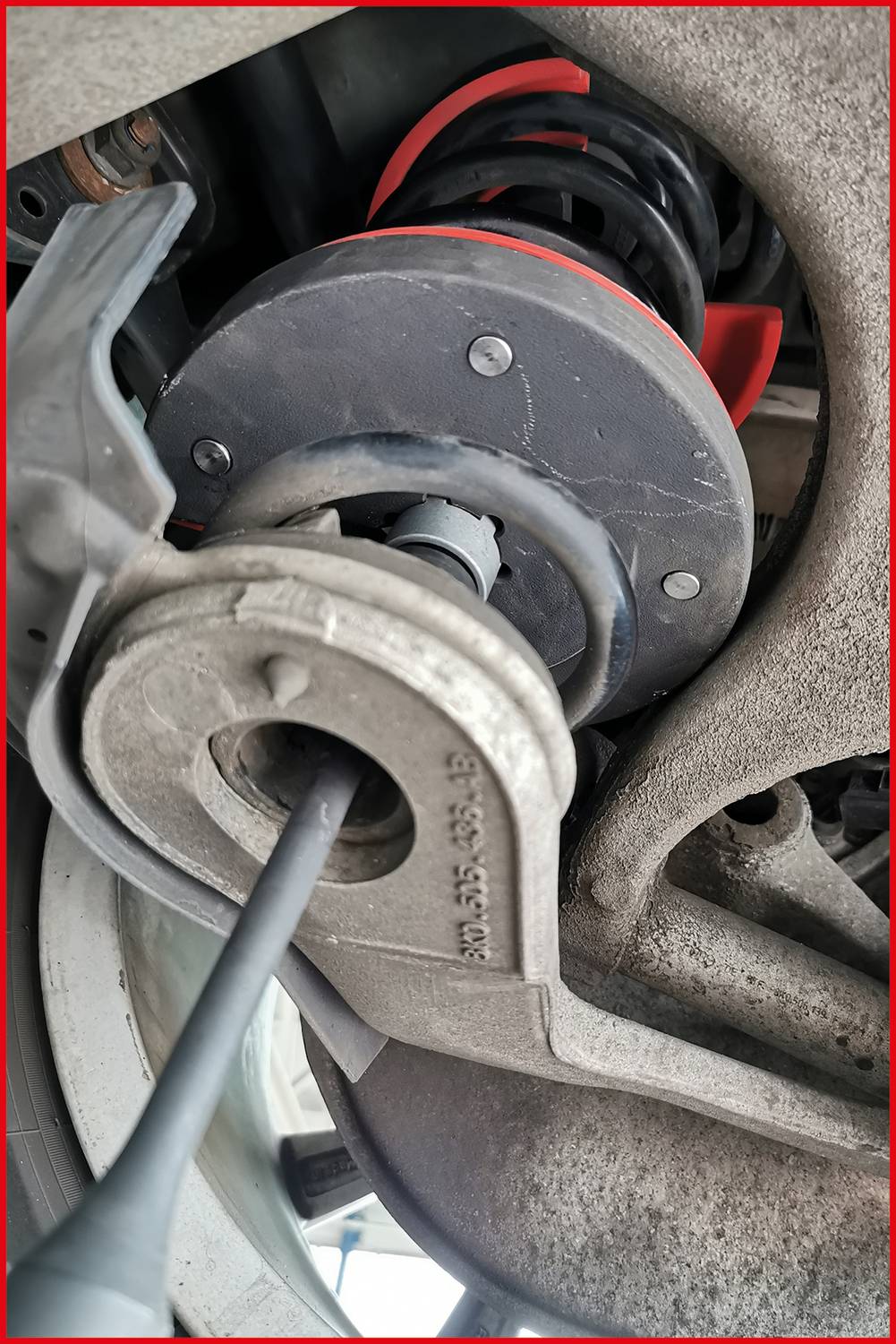 Detailný pohľad na tlmič automobilu v dielni. Technická súčiastka so skrutkami, pružinami a zavesovacími prvkami je viditeľná.