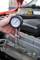 Jedna ruka drží manometer pripojený k automoblovému motoru na meranie tlaku. V pozadí je vidieť priestor motorového priestoru.
