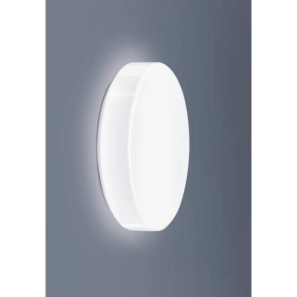Biela, oválna nástenná lampa s difúznym svetlom svieti na sivej stene. Minimalistický dizajn, vhodný pre moderný interiér.