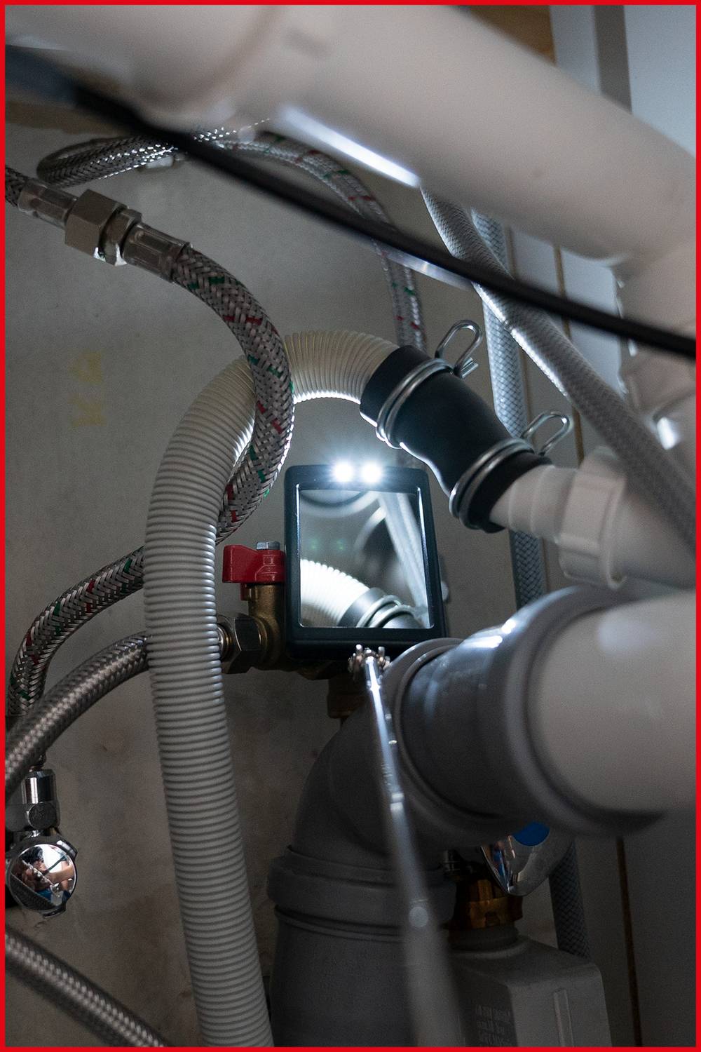 Detailný záber na potrubia a hadice uložené pod umývadlom. Zrkadlo odráža svetlo.