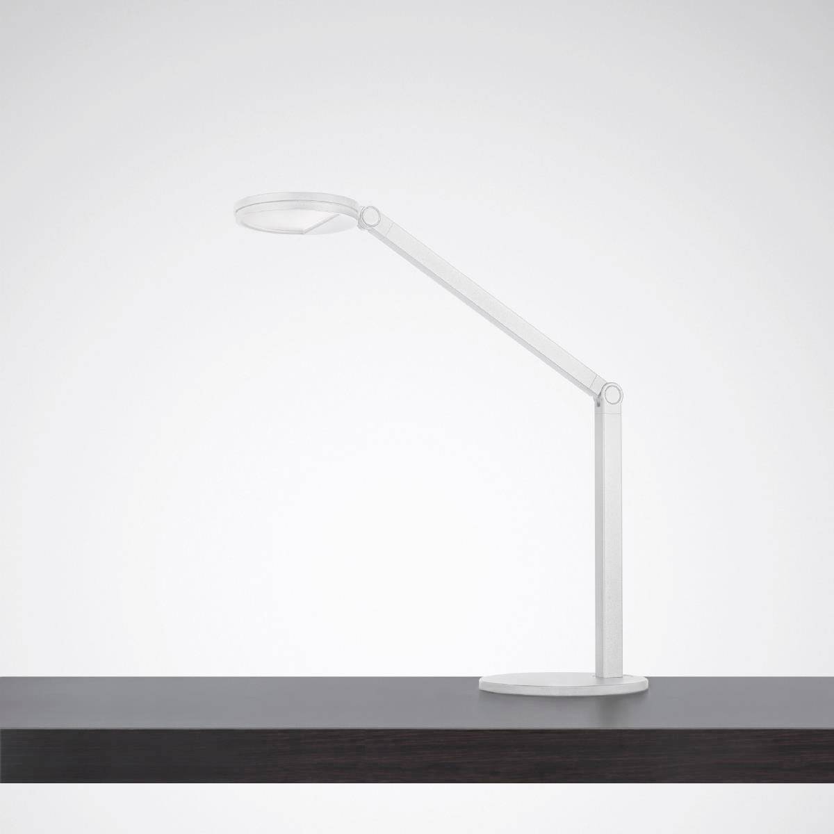 Minimalistická, moderná stolná lampa s ohybným krkom stojí na tmavom drevenom stole pred neutrálnym pozadím.