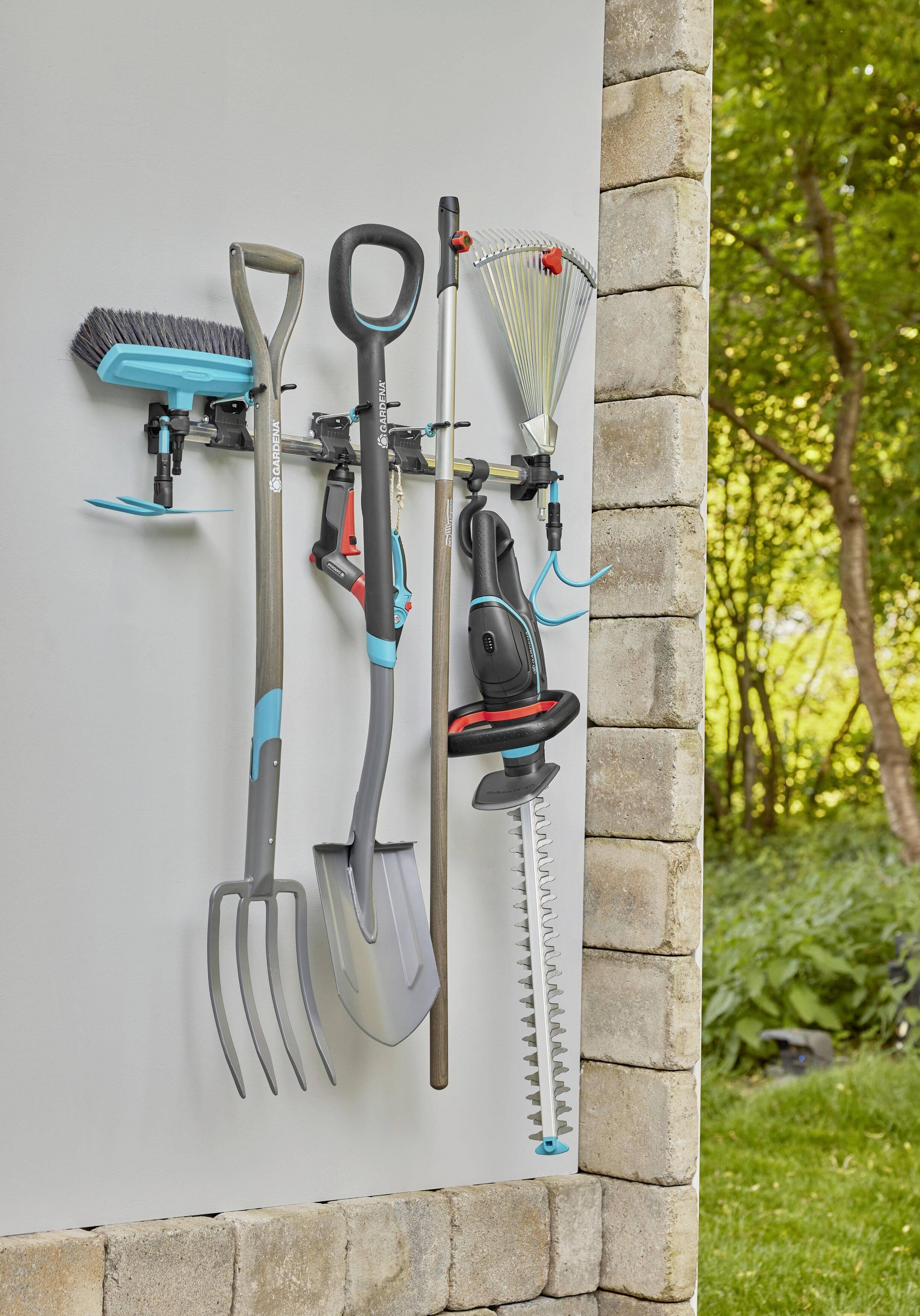 Záhradné náradie ako vidly, lopata, hrable a nožnice na živý plot sú poriadne namontované na stenový držiak v záhrade.