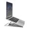 Laptop stojí na nastaviteľnom striebornom stojane, ktorý umožňuje ergonomickú polohu na sledovanie. Obrazovka zobrazuje tmavé používateľské rozhranie.