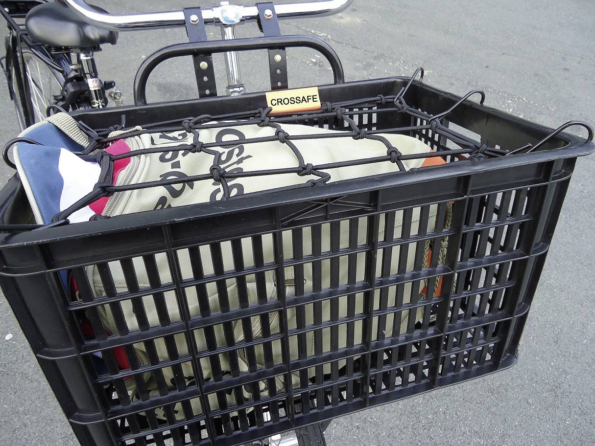 Bicyklový košík s čiernou mriežkou, ktorý obsahuje tašku. Mriežka zaisťuje tašku v košíku, ktorý je pripevnený na stojan na bicykel.