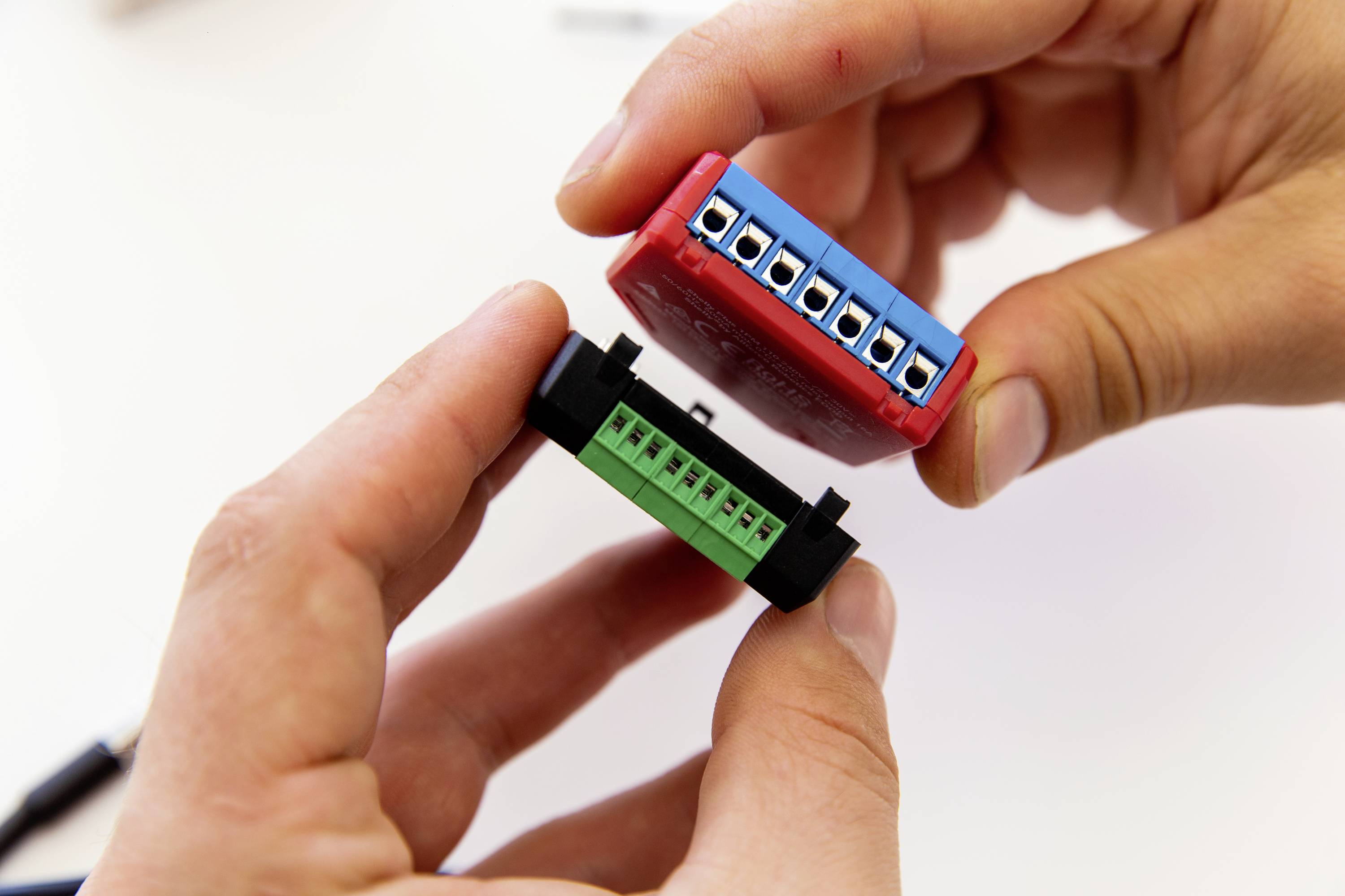 Dve ruky držia elektronické komponenty so farebnými konektormi, ktoré sú pripravené na spájanie.