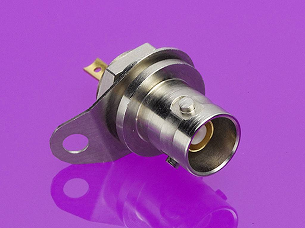 Jeden kovový konektor pred fialovým pozadím. Konektor má kruhovú otvorenú časť a roh s montážnym otvorom.