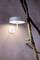 Moderná nástenná lampa svieti na štruktúrovanej stene vedľa konára pokrytého machom.
