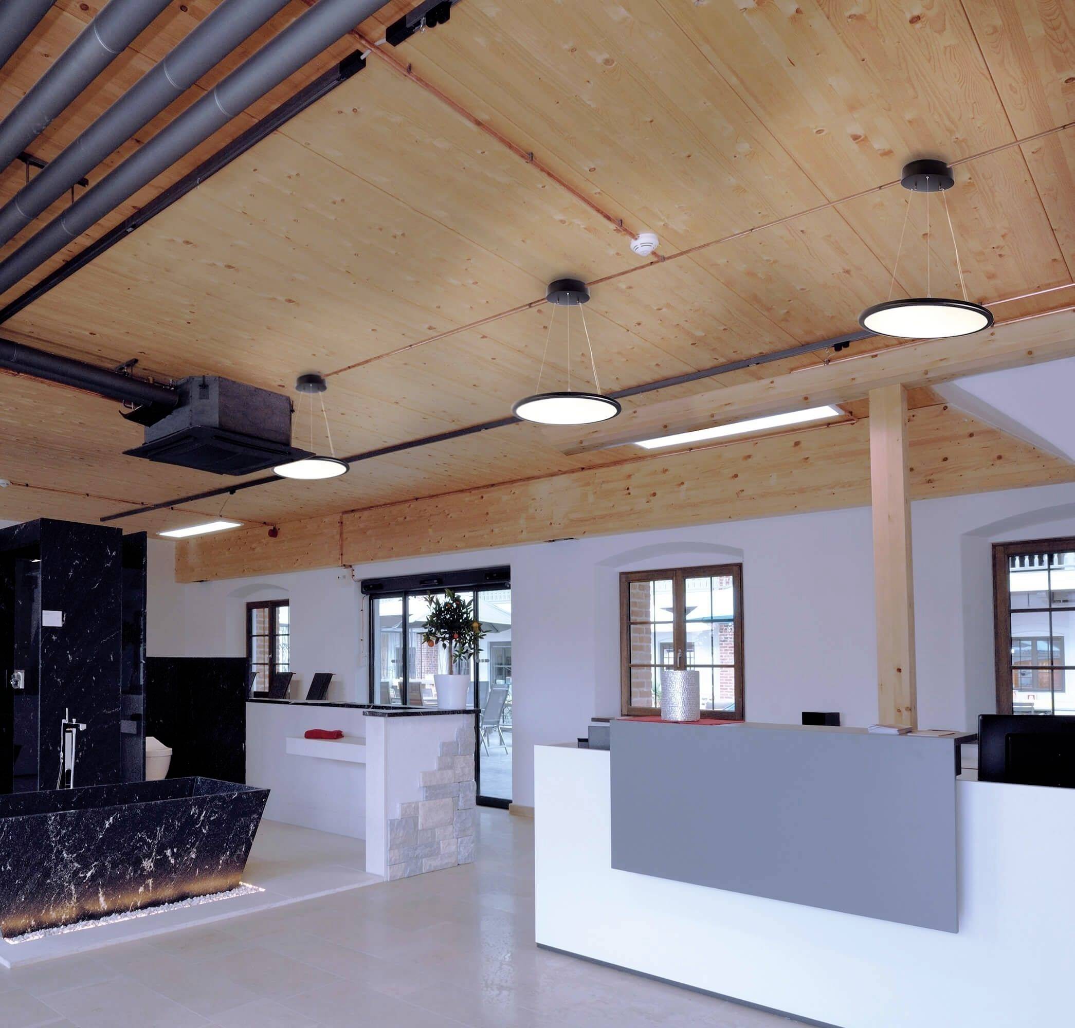 Moderná kancelária s dreveným trámovým stropom, svetlými stenami a mramorovým recepčným pultom. Závesné lampy vytvárajú teplé osvetlenie.