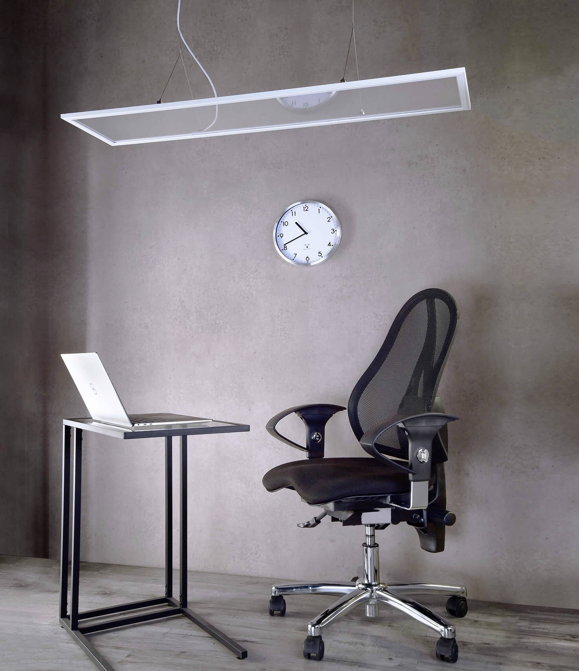 Moderné pracovisko s laptopom na úzkom stole, ergonomickou čiernou kancelárskou stoličkou a závesným hodinám v minimalistickom priestore.