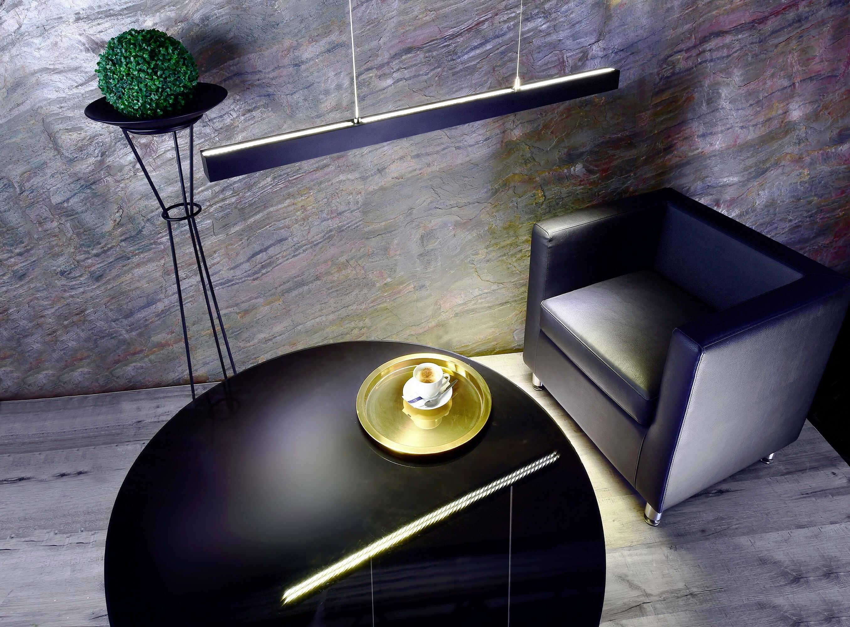 Moderný lounge priestor s čiernym kreslom, okrúhlym čiernym stolíkom a zlatým podnošom s šálkou kávy.