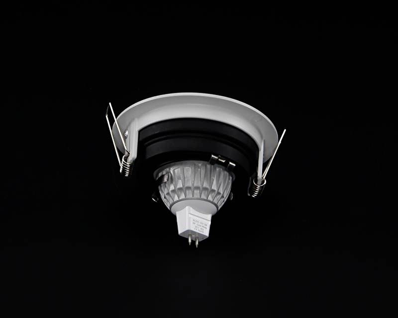 Vstavaná LED lampa v čierno-bielom kryte, s dvoma kovovými svorkami na upevnenie na strope, pred čiernym pozadím.