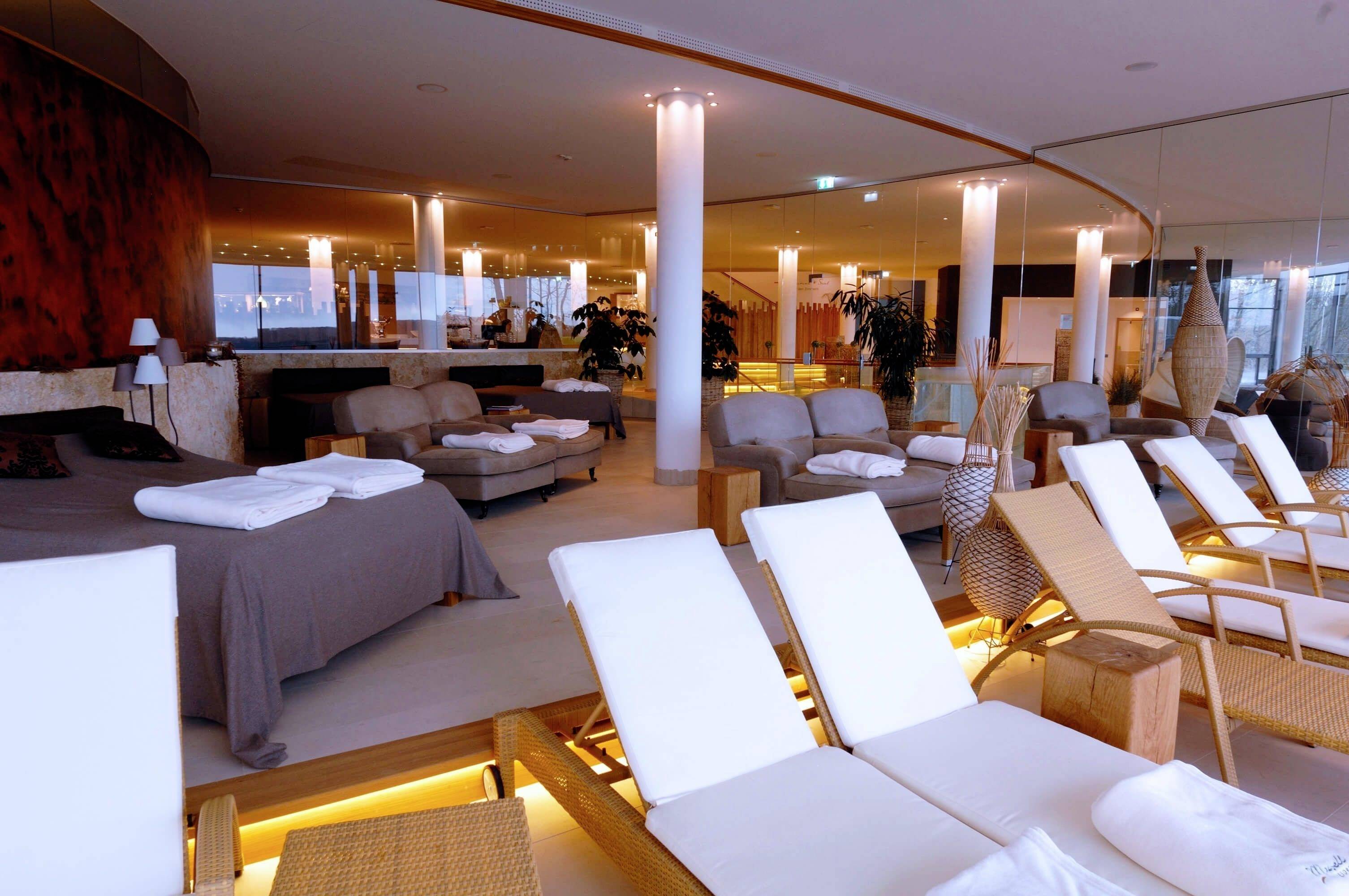 Wellness priestor s ležadlami a pohodlnými sedacími zónami, obklopený jemným osvetlením a rastlinami, navodzuje pocit relaxácie.