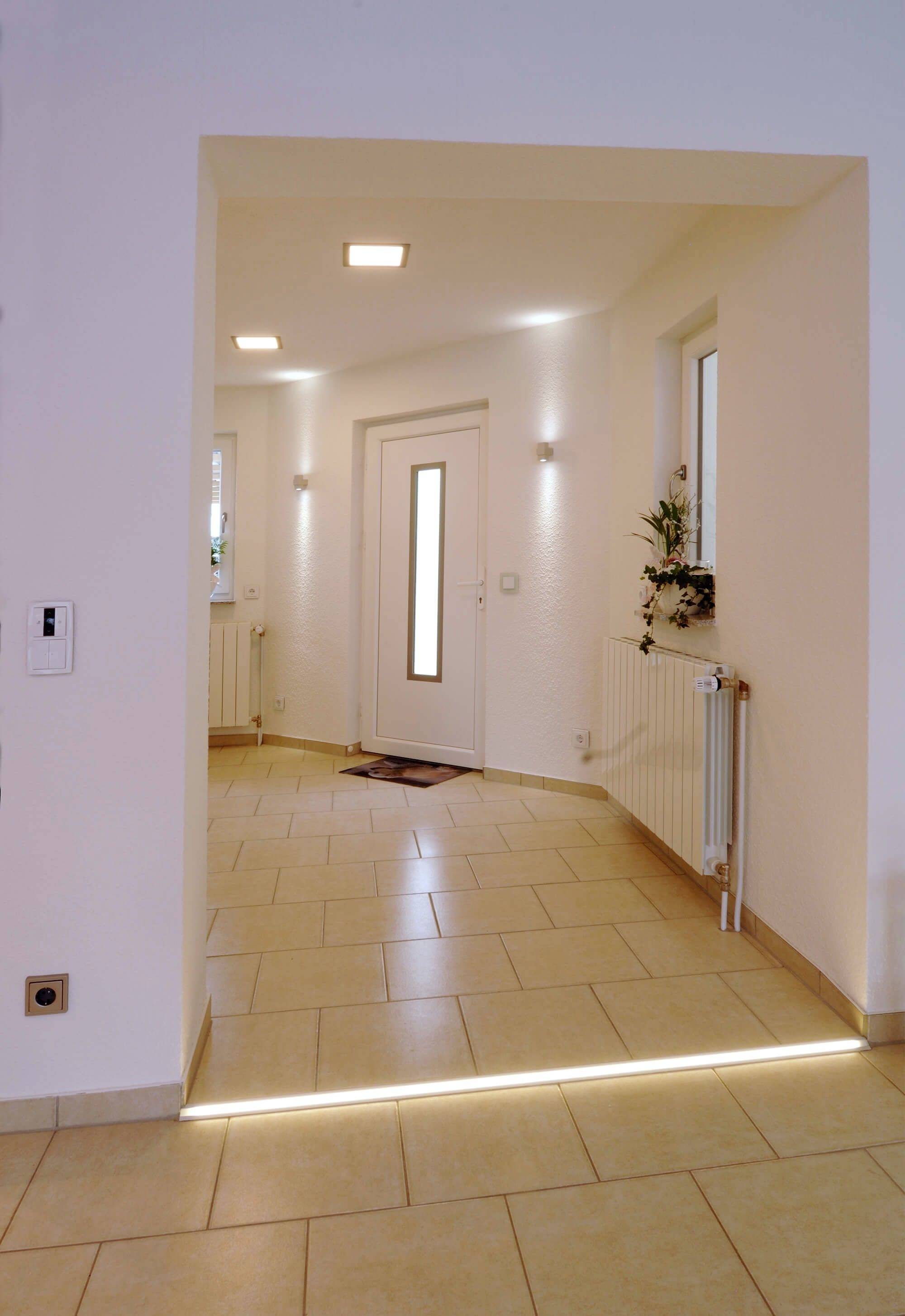 Vstupný priestor s jasnou dlažbou, bielymi dverami a moderným konceptom osvetlenia. Rastliny na parapete vedľa radiátora.