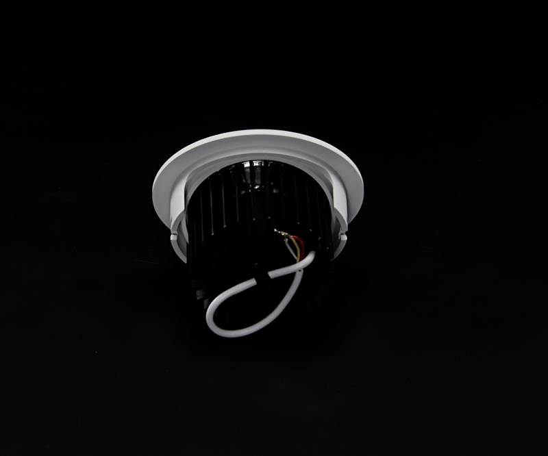 Jeden LED stropný podhľadový reflektor s čiernym chladičom a bielymi káblami pred čiernym pozadím.