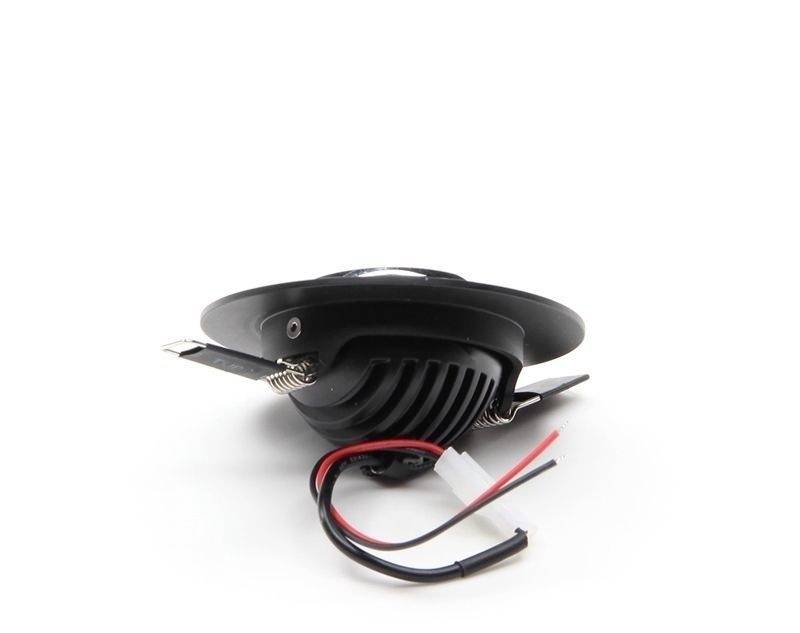 Okrúhle LED svetlo s čiernym puzdrom a vyčnievajúcimi drôtmi. Leží na bielom povrchu, pohľad zboku.