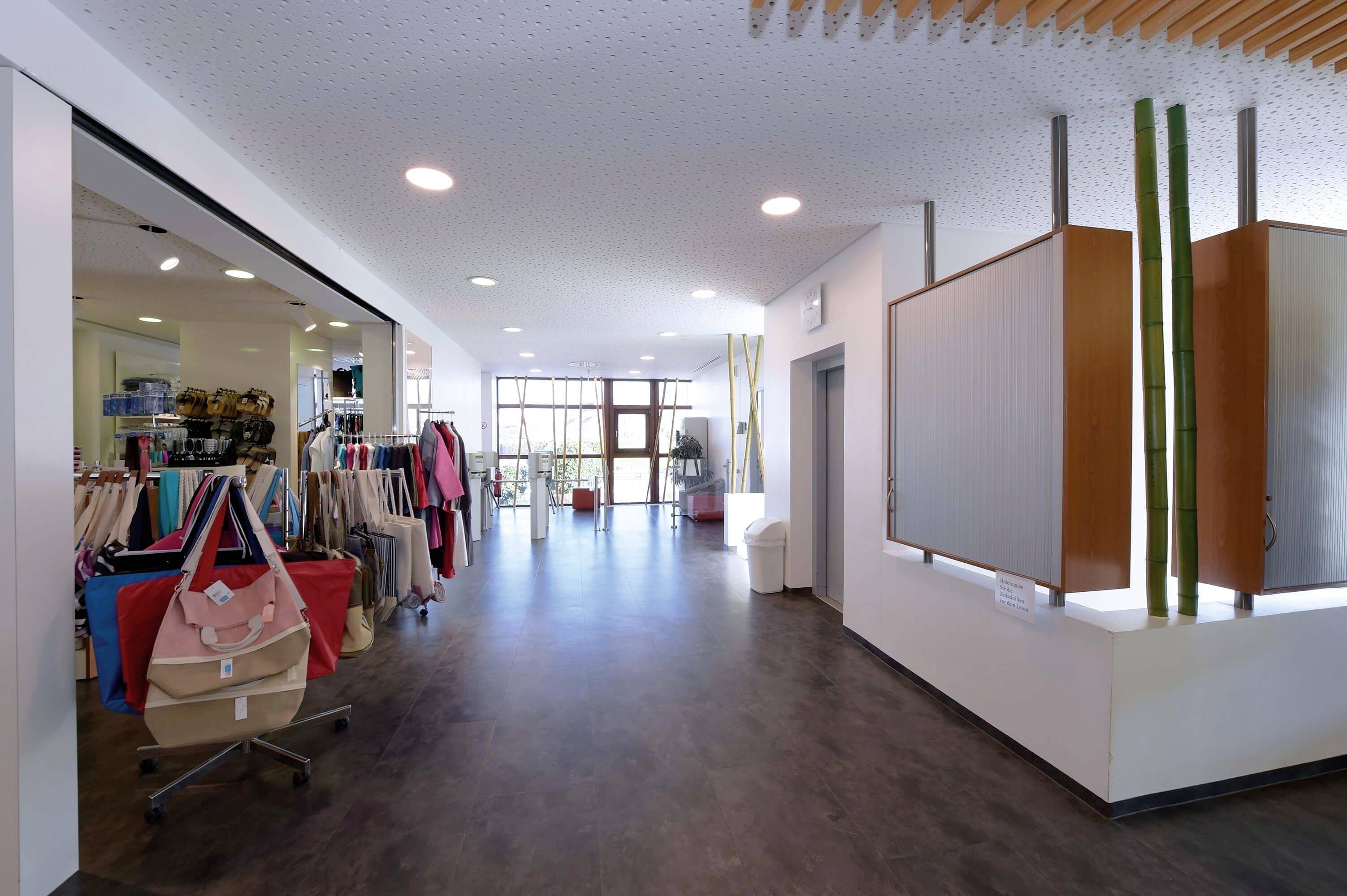 Interiér obchodu s políčkami plnými farebných tašiek a doplnkov na ľavej strane, moderný recepčný priestor v pozadí.