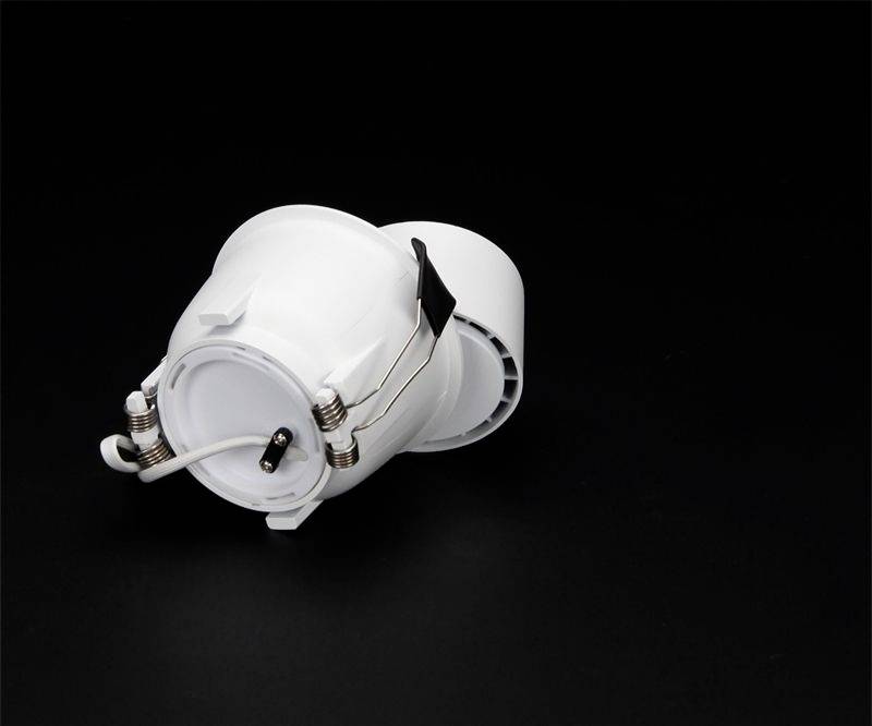 Biele LED svietidlo so zdrojom svetla GU10 leží na čiernej ploche. Podsvietenie zvýrazňuje štruktúru plastu.