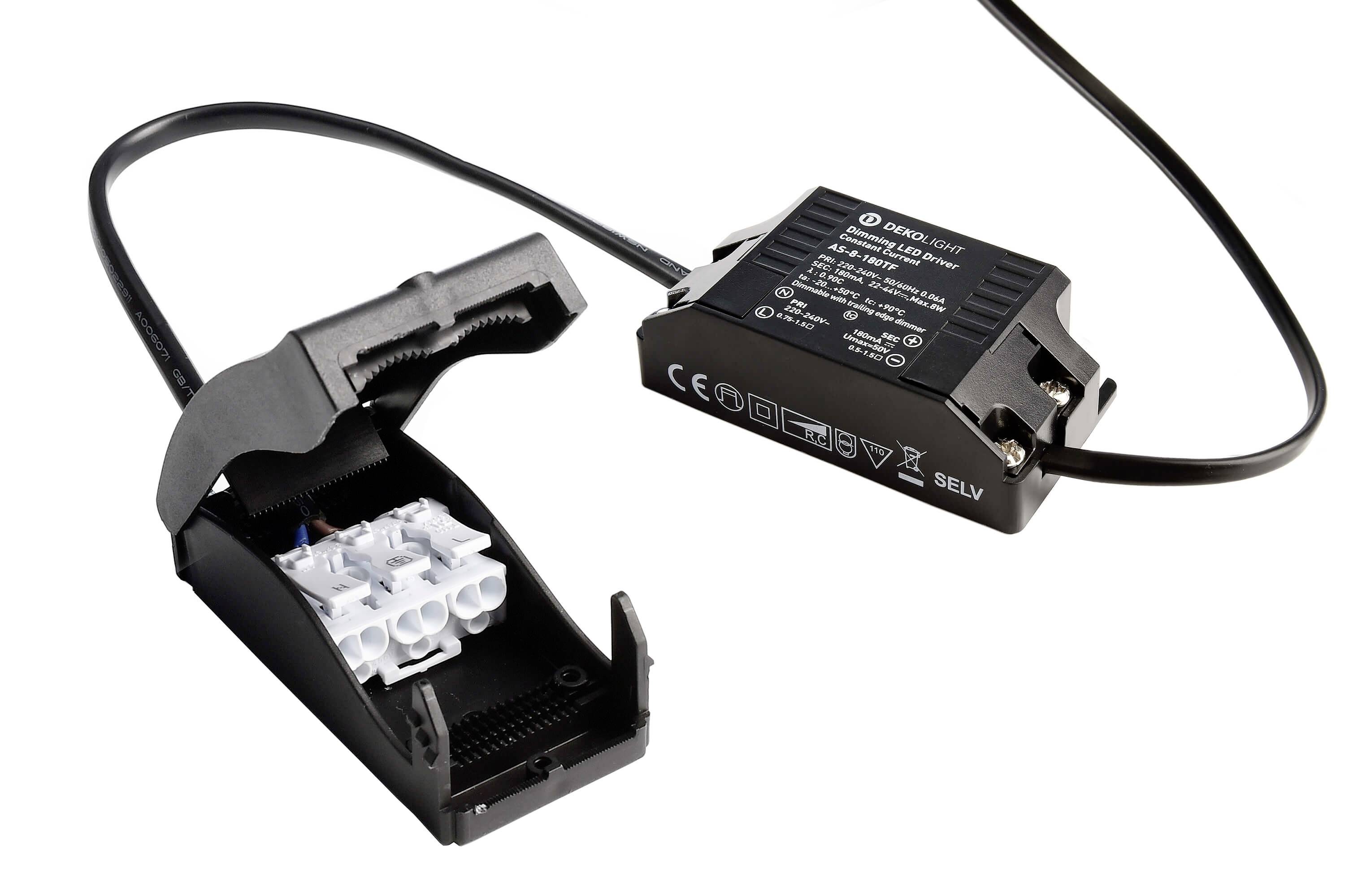 Otvorený čierny plastový kryt s viditeľnými bielymi svorkami je pripojený k čiernemu elektrickému transformátoru.