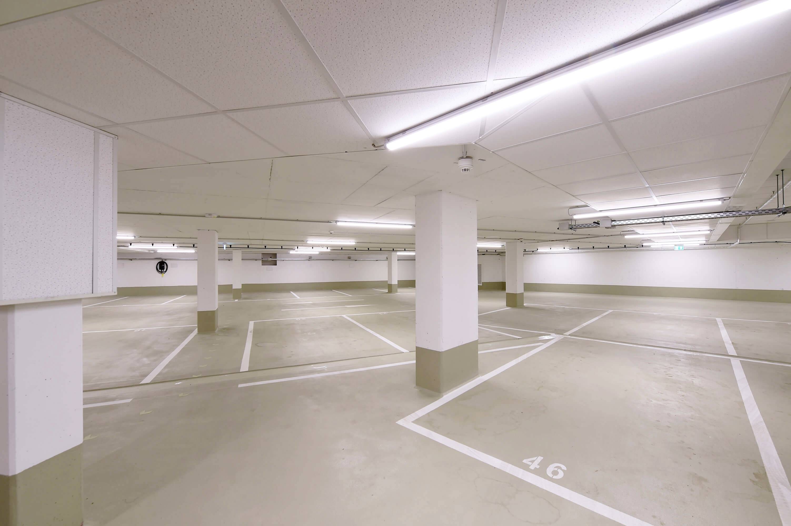 Prázdne, dobre osvetlené podzemné parkovisko s niekoľkými vyznačenými parkovacími miestami a šípkami na podlahe.