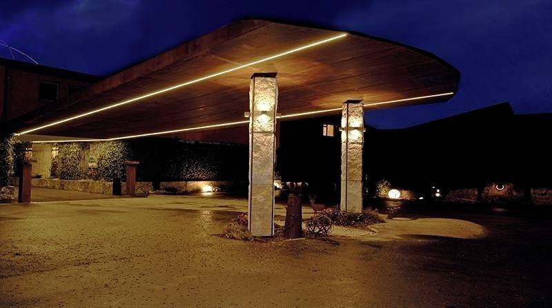 Moderná markíza v nočnej dobe s teplým svetlom, ktorú nesú dva kamenné stĺpy, osvetľuje elegantný vstupný priestor.