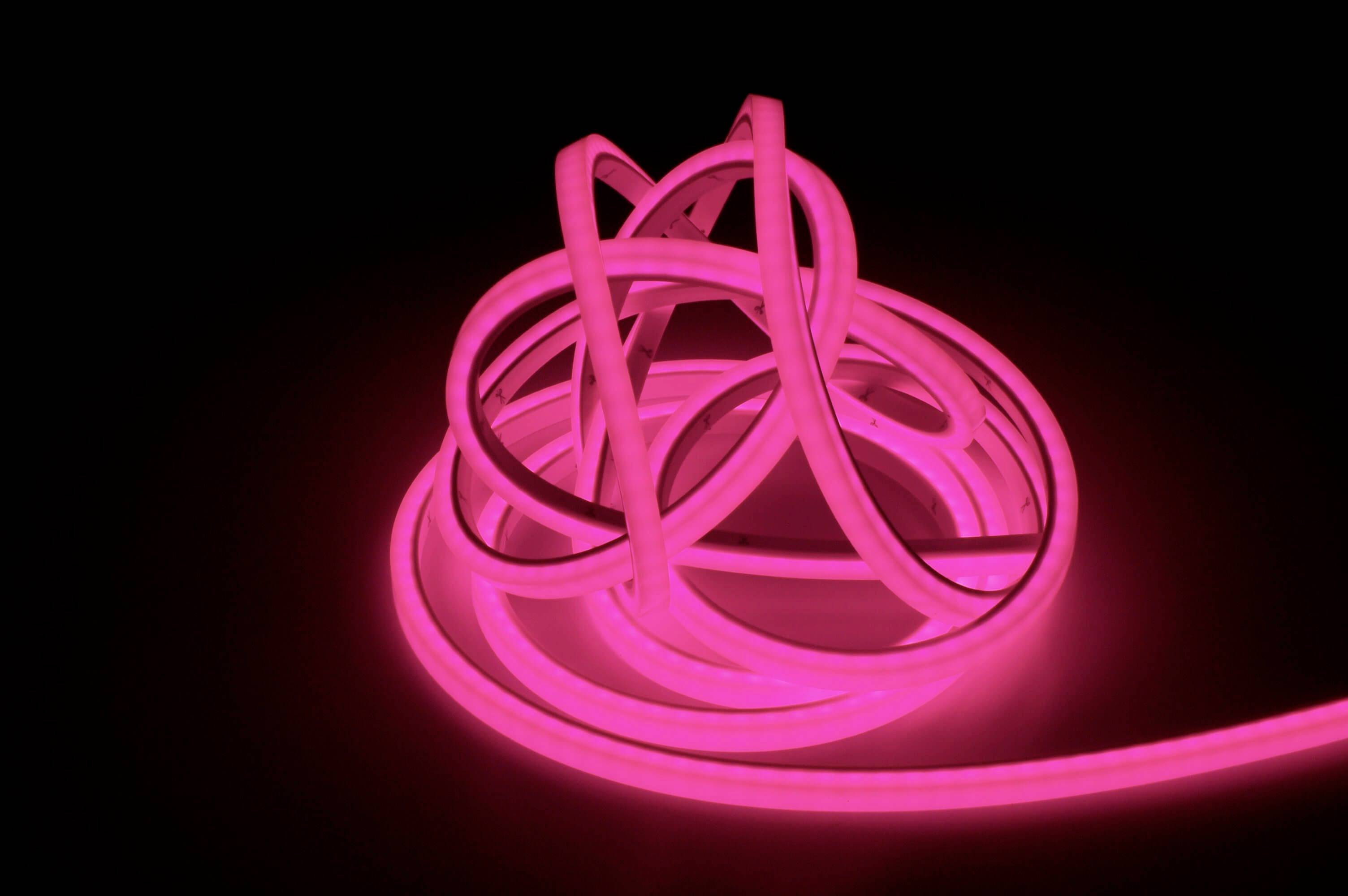 Svetelný, ružový LED pás je umelecky naaranžovaný do voľnej slučky na čiernom pozadí.