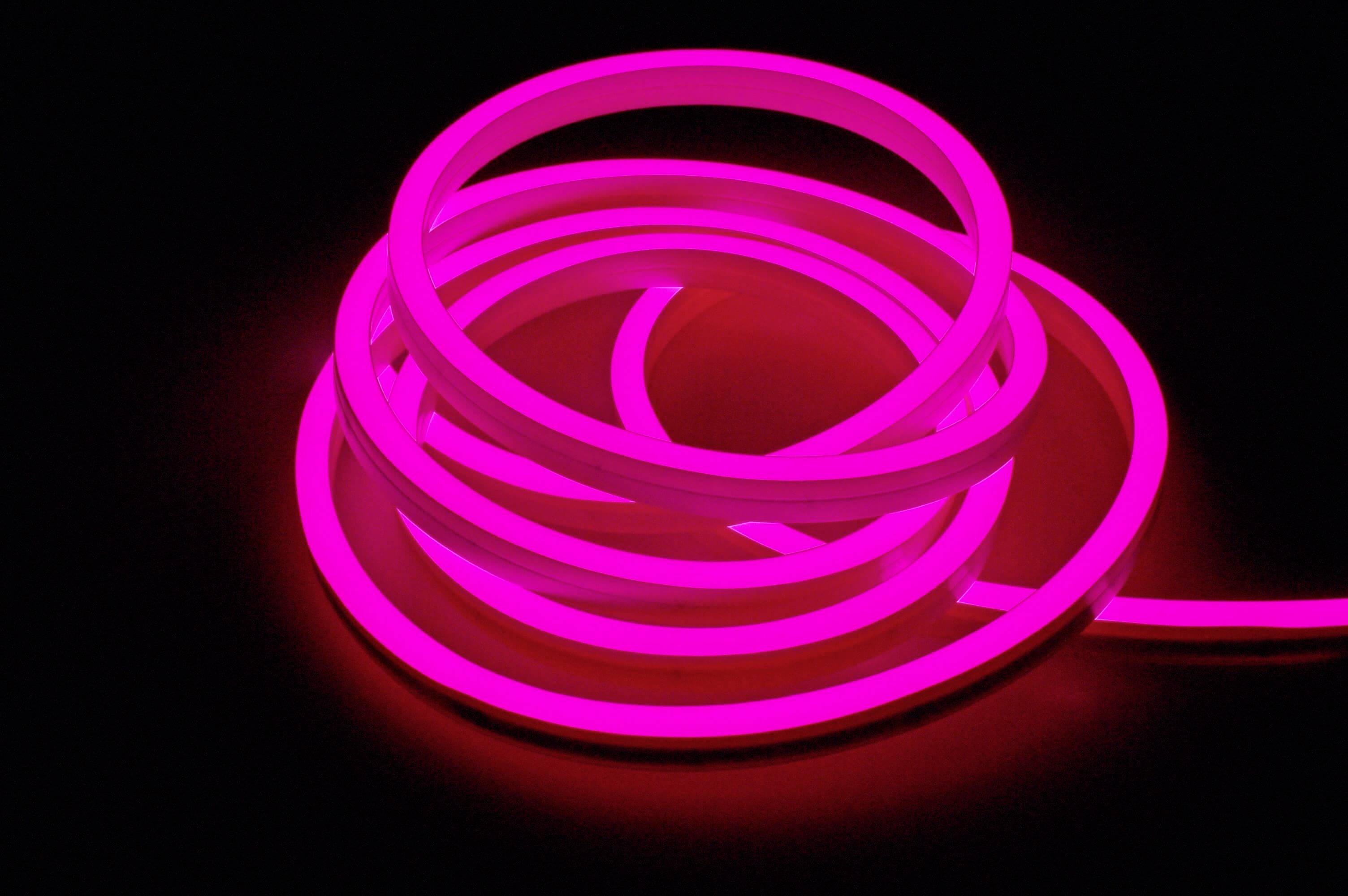 Žiarivý, ružový neónový pruh, ktorý je niekoľkokrát voľne omotaný na tmavom pozadí.