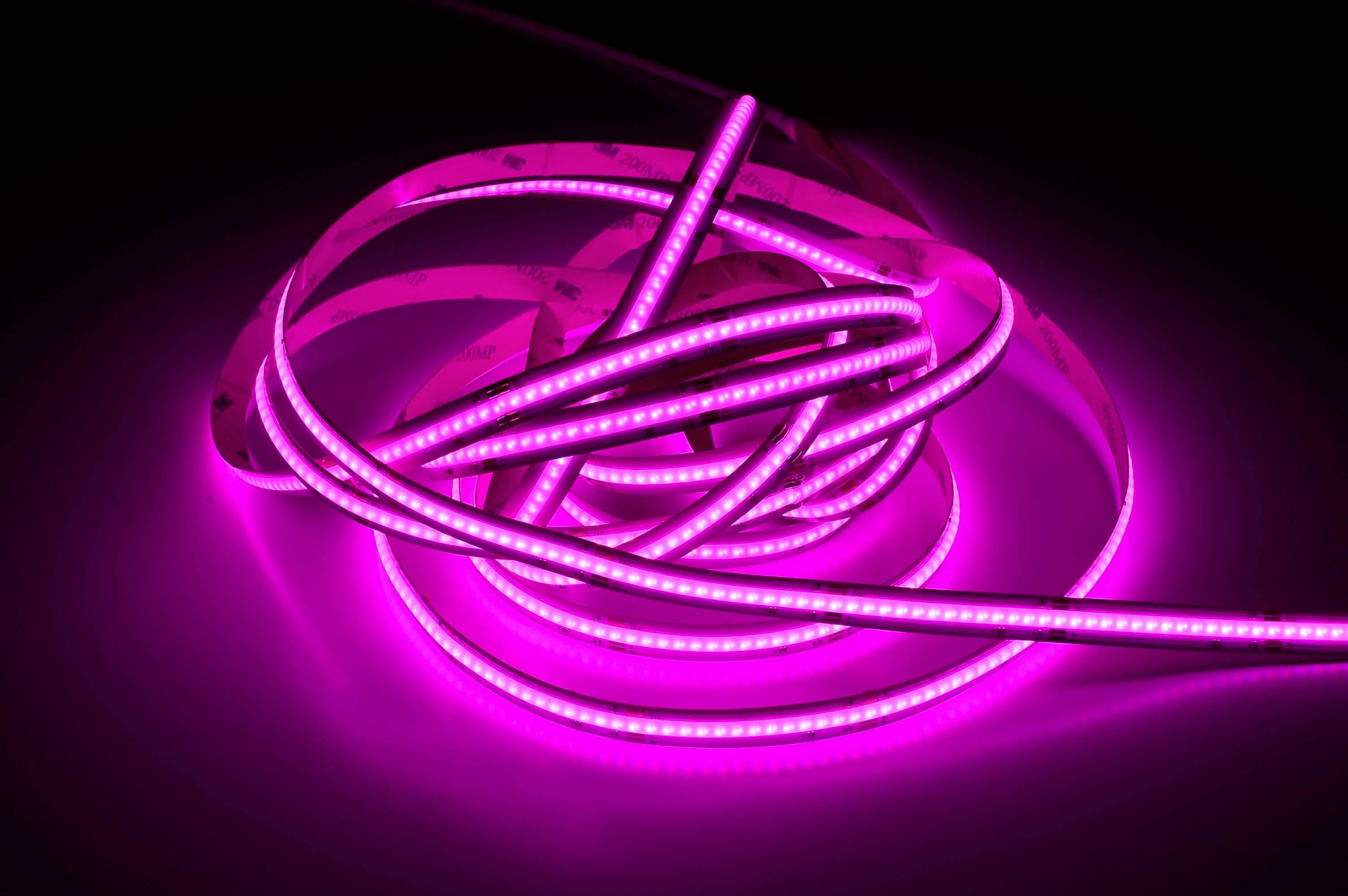 Svetielkujúce, ružové LED svetelné pásy voľne ležia na tmavom povrchu. Vyžarujú mäkké, farebné svetlo.