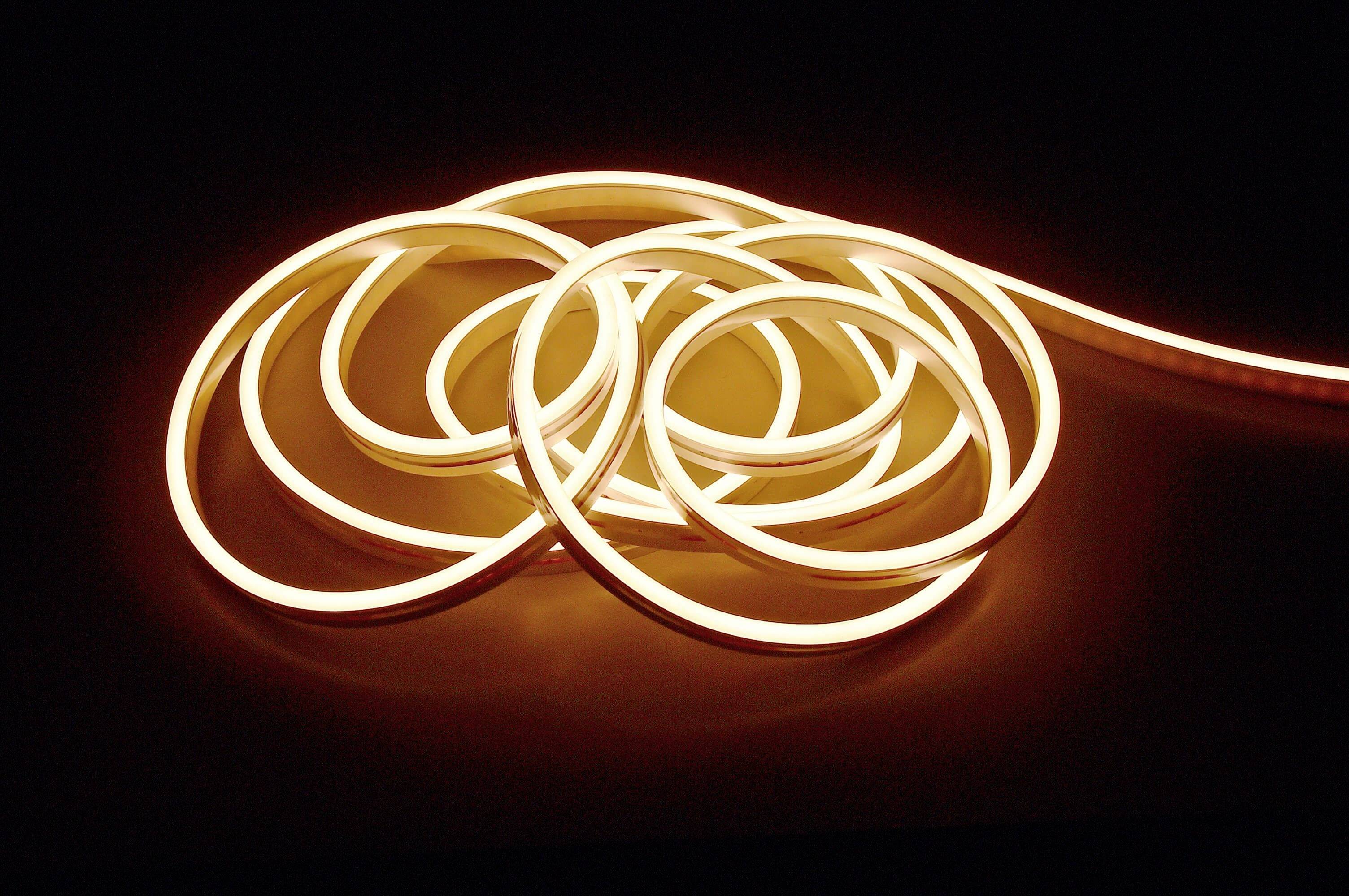 Stočený LED pás svieti teplou žltou farbou na čiernom pozadí.