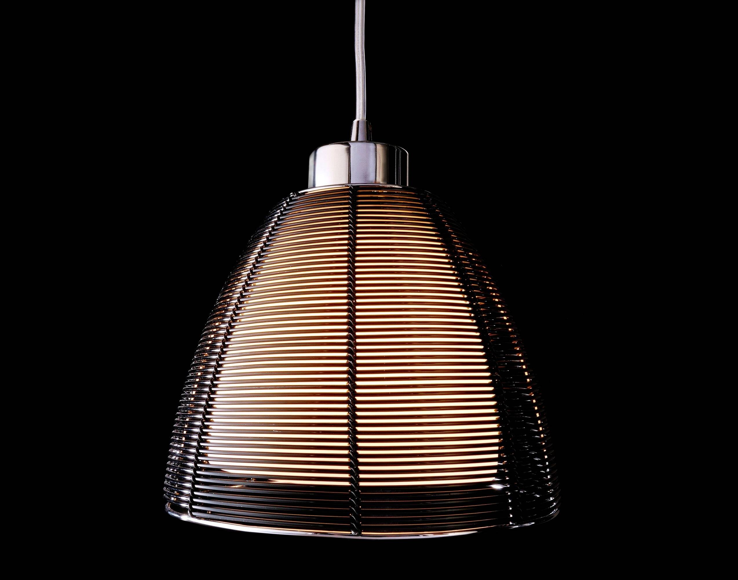 Moderná závesná lampa s okrúhlymi horizontálnymi kovovými pruhmi okolo tienidla, ktorá teplým svetlom žiari pred čiernym pozadím.