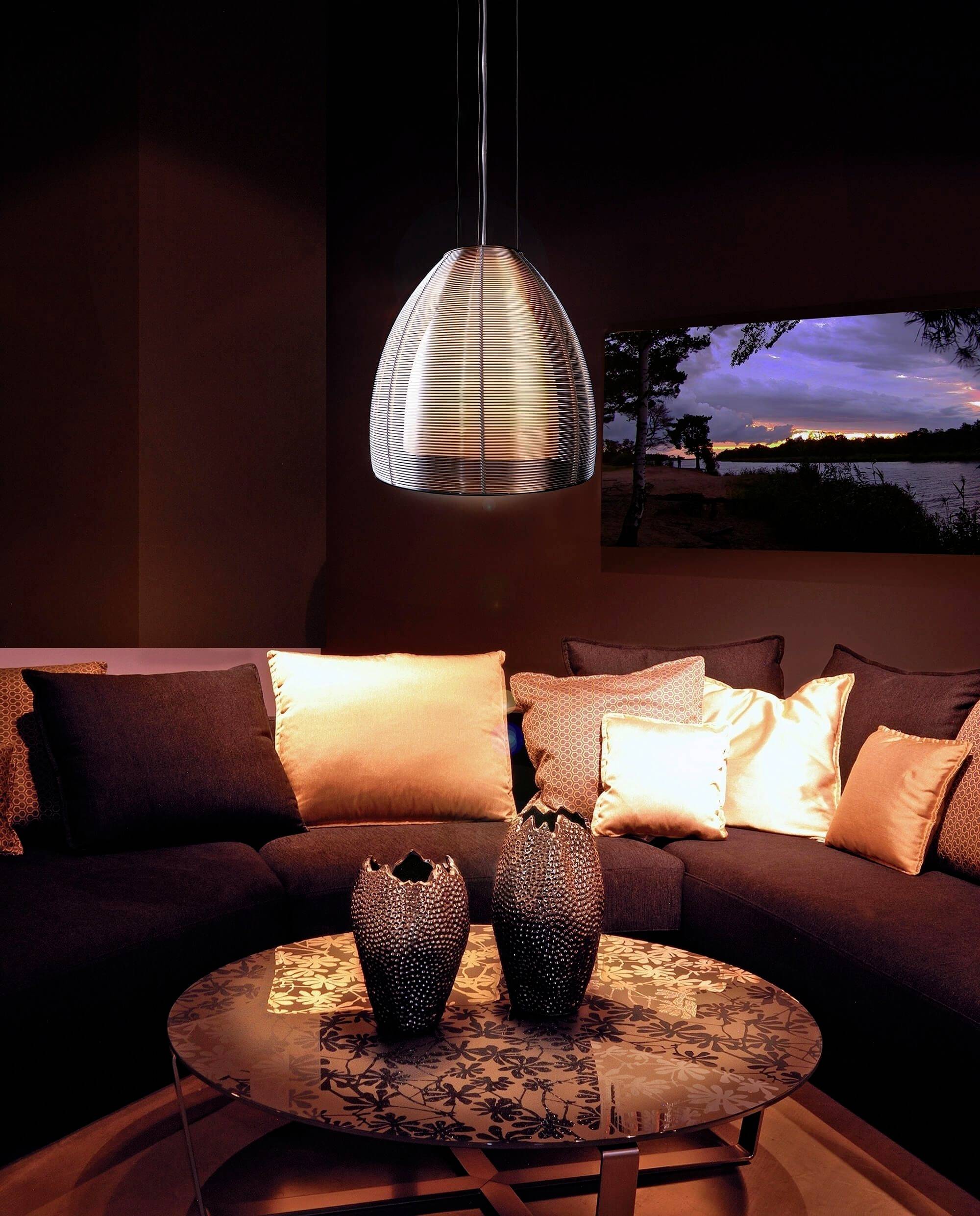 Útulná obývačka za súmraku s elegantnou závesnou lampou nad konferenčným stolíkom, ozdobená vázami pred pohovkovým sedením.