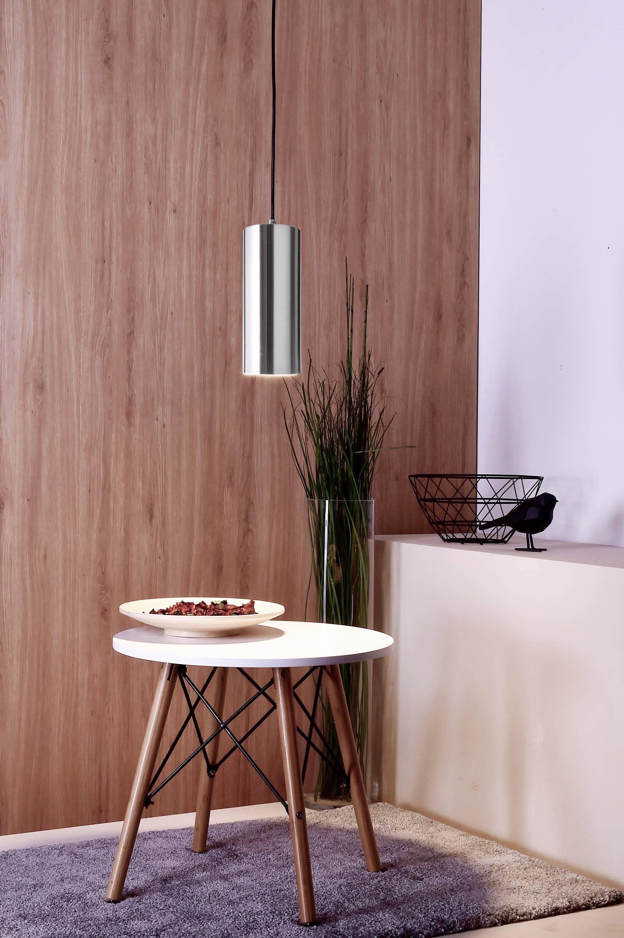 Malý okrúhly stôl s drevenými nohami stojí na koberci. Na ňom je tanier s čokoládou. Nad stolom visí závesná lampa.