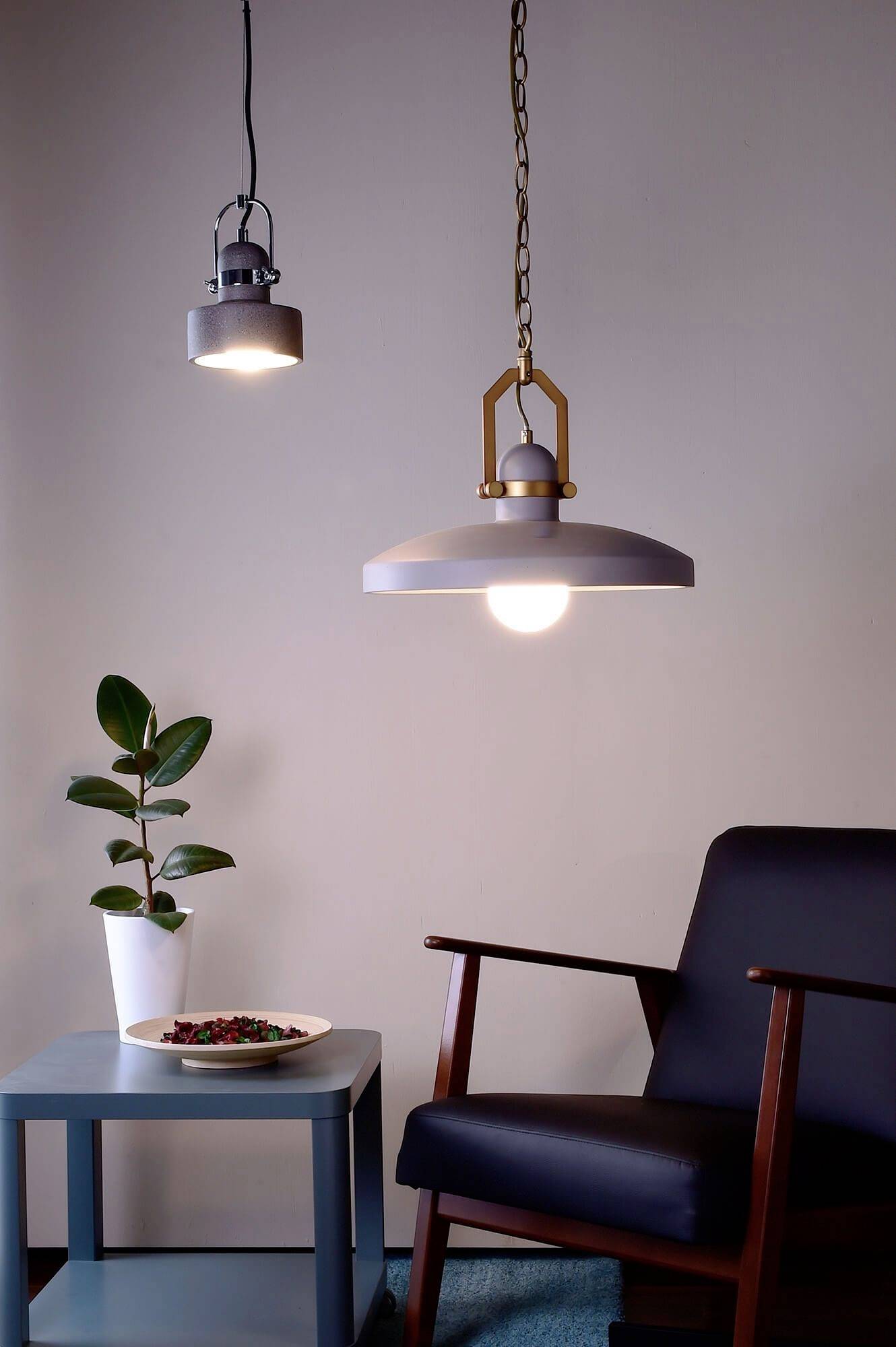 Útulná obývačka s kreslom, vedľajším stolíkom s rastlinou a dvoma visiacimi lampami.