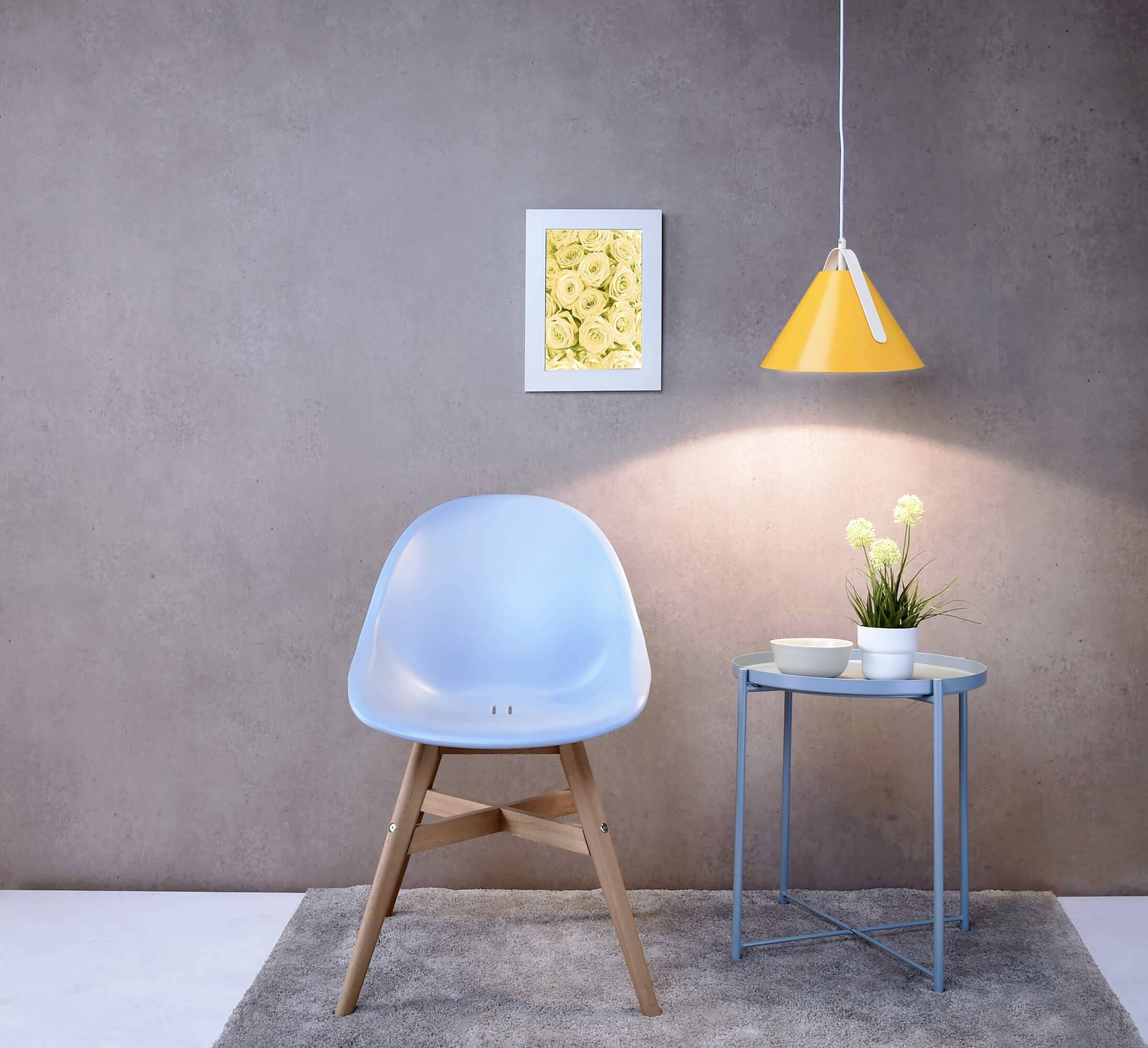 Modrá stolička stojí na koberci pred šedou stenou. Vedľa stoličky je malý stolík s rastlinami a riadom.