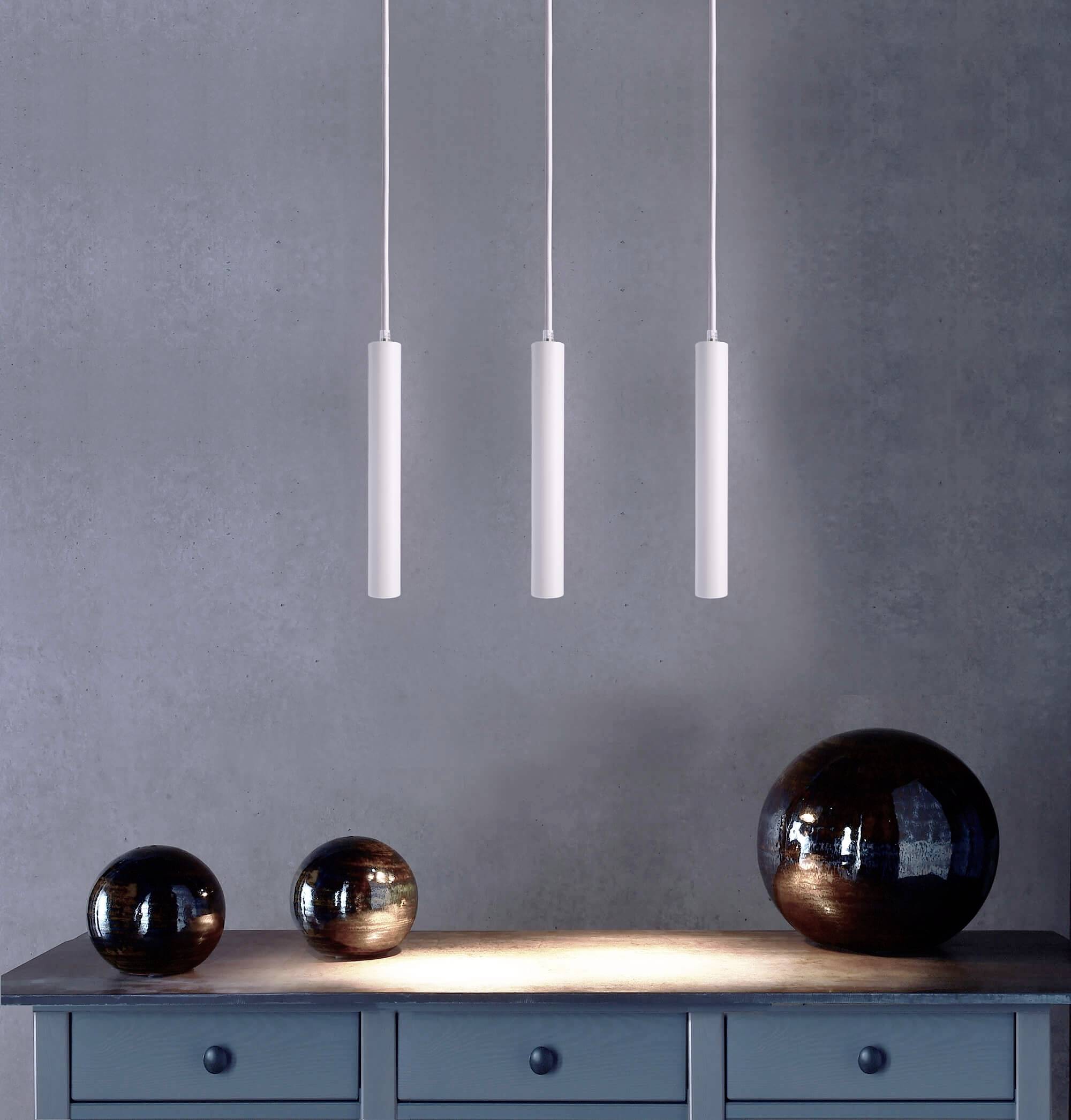 Tri minimalistické biele závesné svietidlá nad modrým skleneným príborníkom s okrúhlymi tmavými dekoratívnymi guľami.