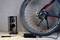 Bicykel stojí pri stene, je vidieť zadné koleso. Vedľa je nabíjacia stanica s zapojenou batériou.