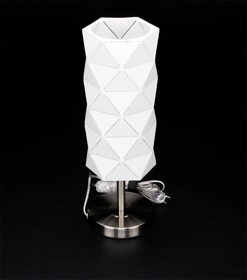 Moderná stolná lampa s geometrickým bielym tienidlom na striebornom podstavci pred čiernym pozadím.