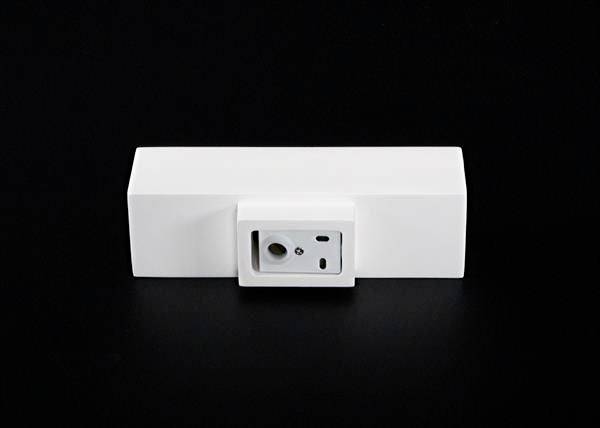 Biela elektronická zariadenie na čiernom pozadí, pravdepodobne senzor alebo kamera, štvorcového tvaru s šošovkou v strede.