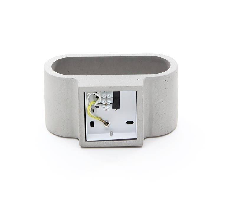 Sivý, oválny betónový podstavec lampy so viditeľnými elektrickými prípojkami a káblami vo vnútri, otvorený dizajn určený na montáž na stenu.