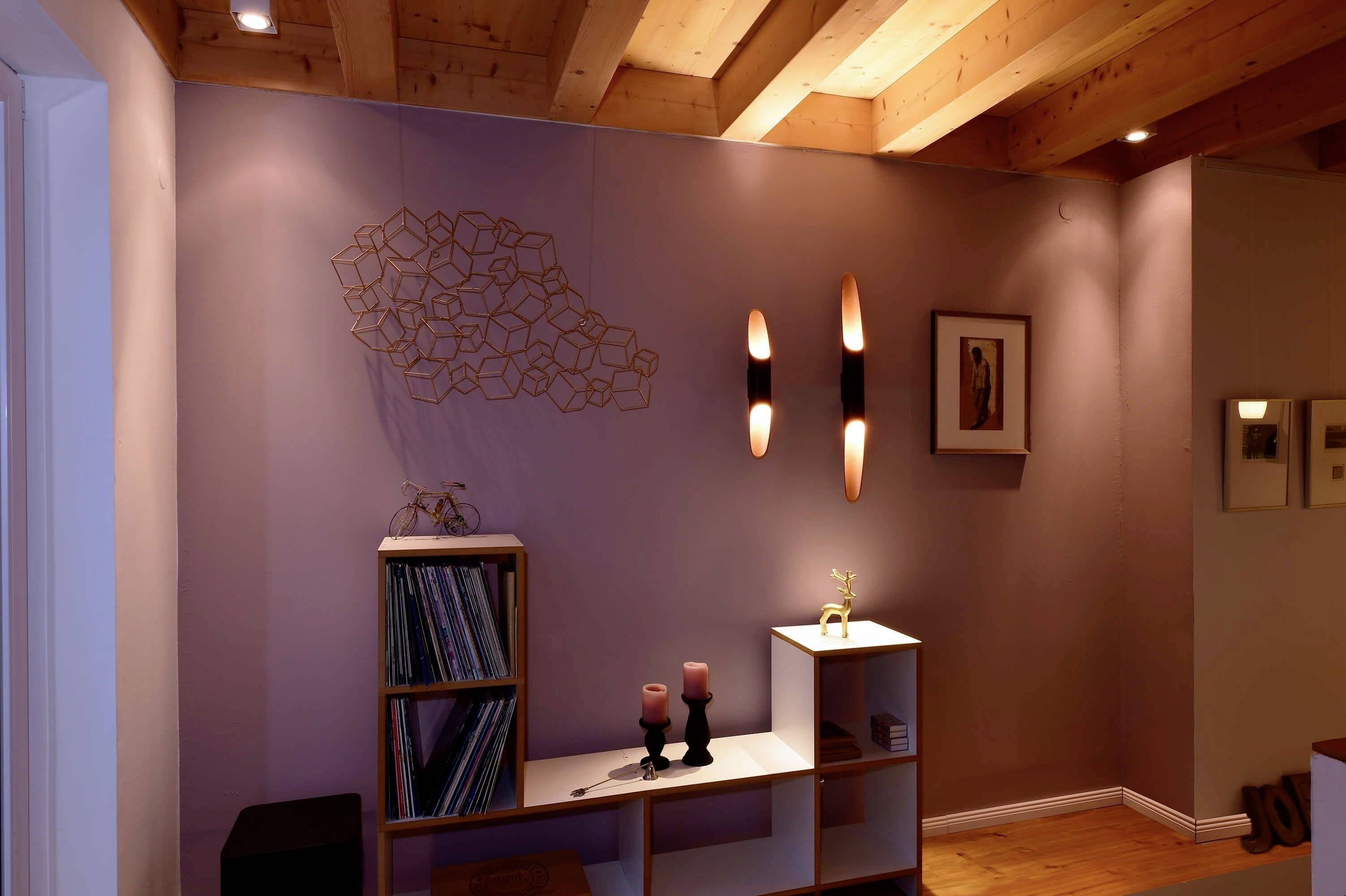 Útulná obývacia izba so stropom s drevenými trámami. Na stene sú zavesené umelecké diela a osvetlenie. Polica obsahuje vinylové platne a dekorácie.