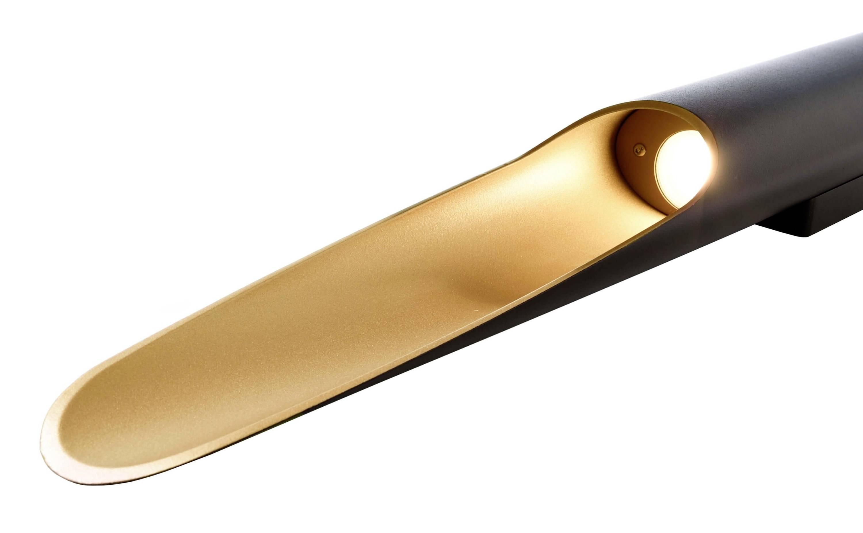 Moderná lampa s úzkym, čiernym plášťom a zlatým vnútrom, ktoré vyžaruje nepriame svetlo cez otvor.