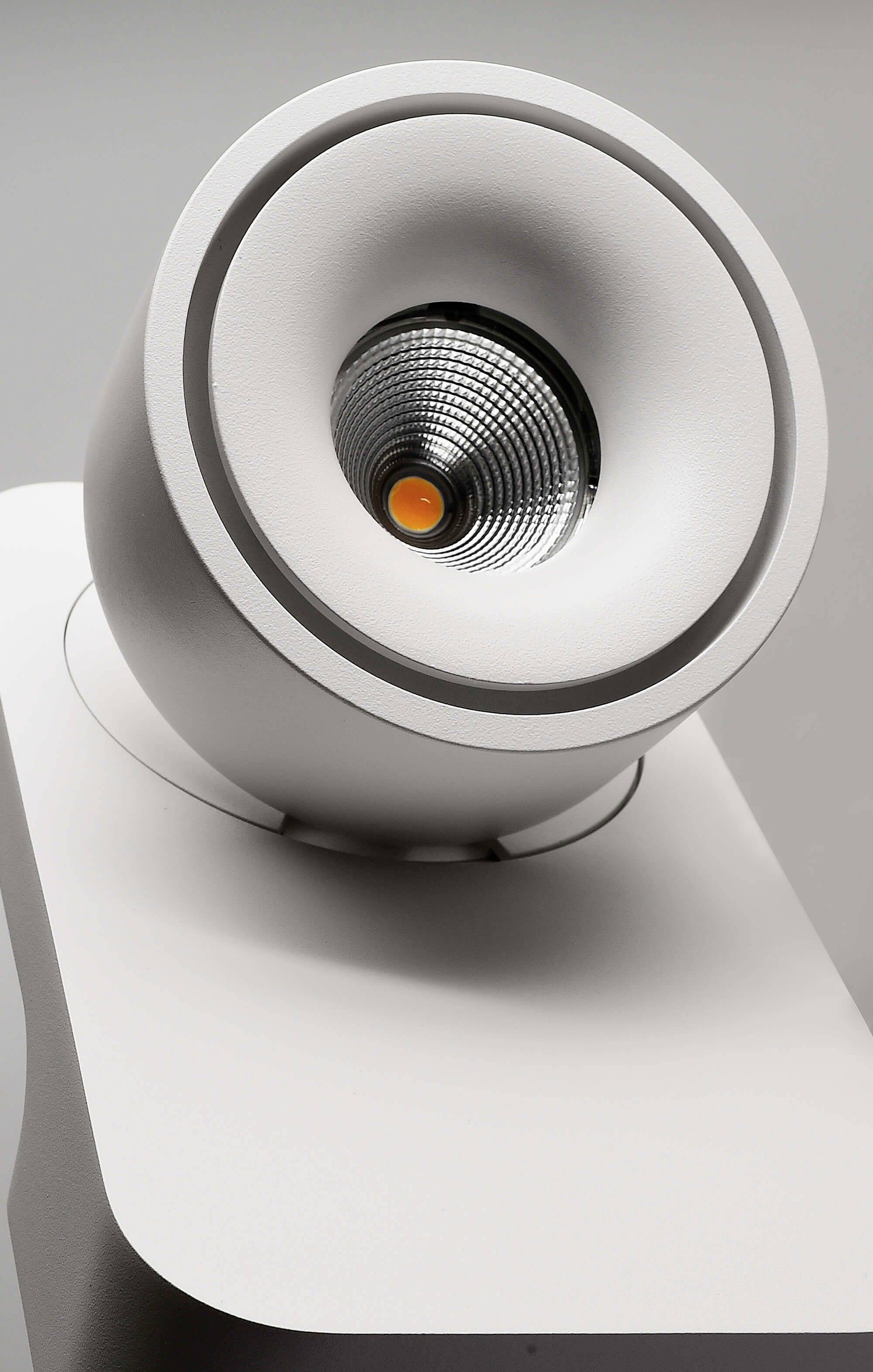 Moderná, biela, okrúhla LED lampa v detailnom zábere, mierne naklopená smerom doprava hore.