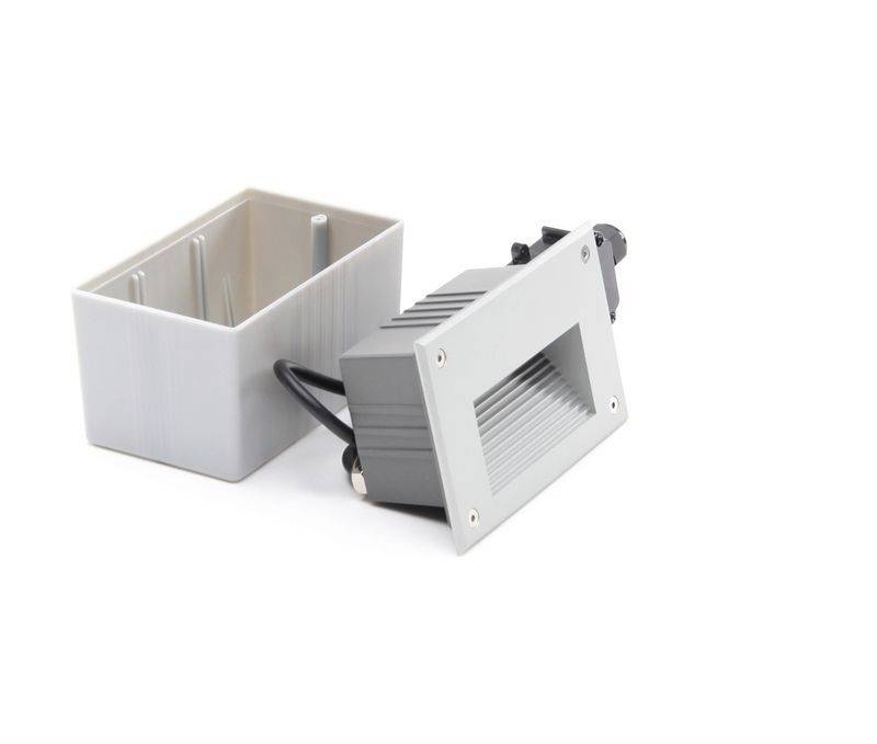 Obdĺžnikový sivý žiarič s káblom, oprený o bielu montážnu krabicu. Vhodný na zabudovanie do stien alebo podláh.