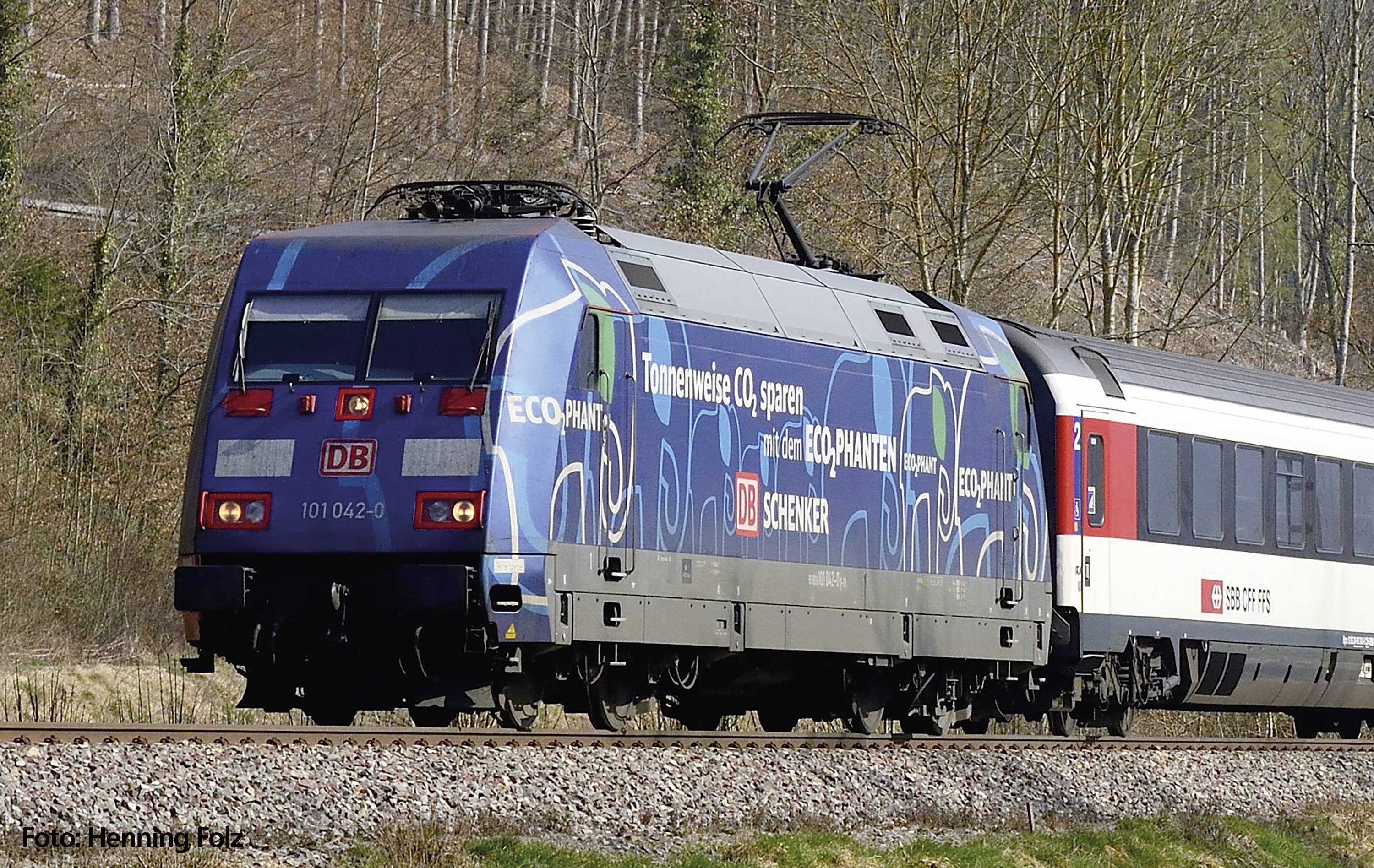 Moderný vlak Deutsche Bahn ide po koľaji cez vidiecku krajinu. Lokomotíva je nalakovaná na modro.